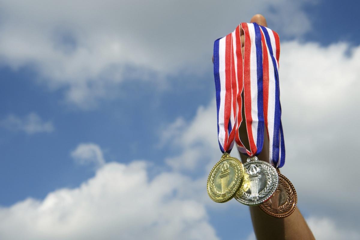 3 medallas tomadas de una mano, con fondo de cielo.