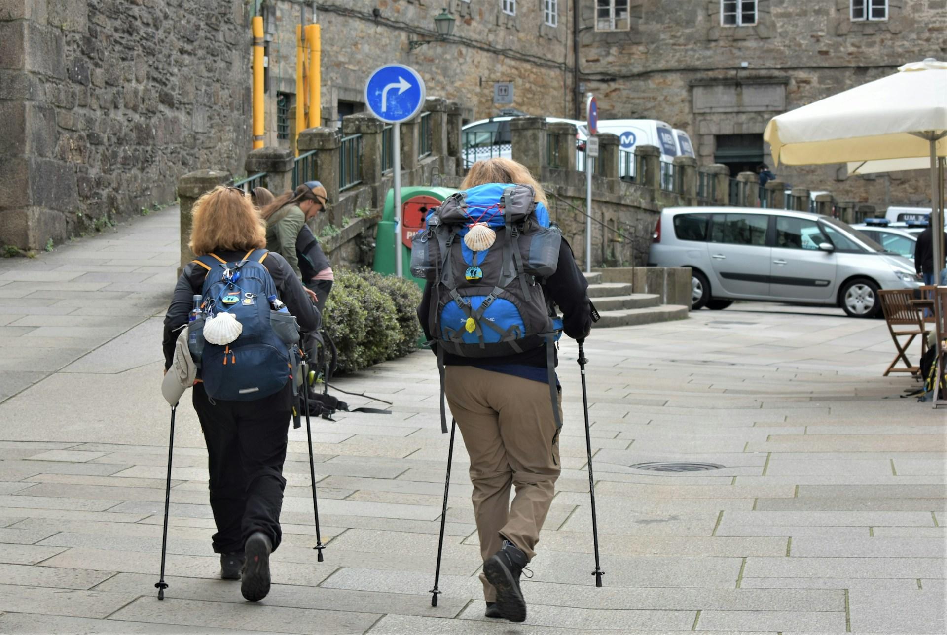 Dos mujeres peregrinas caminando con mochilas y bastones.