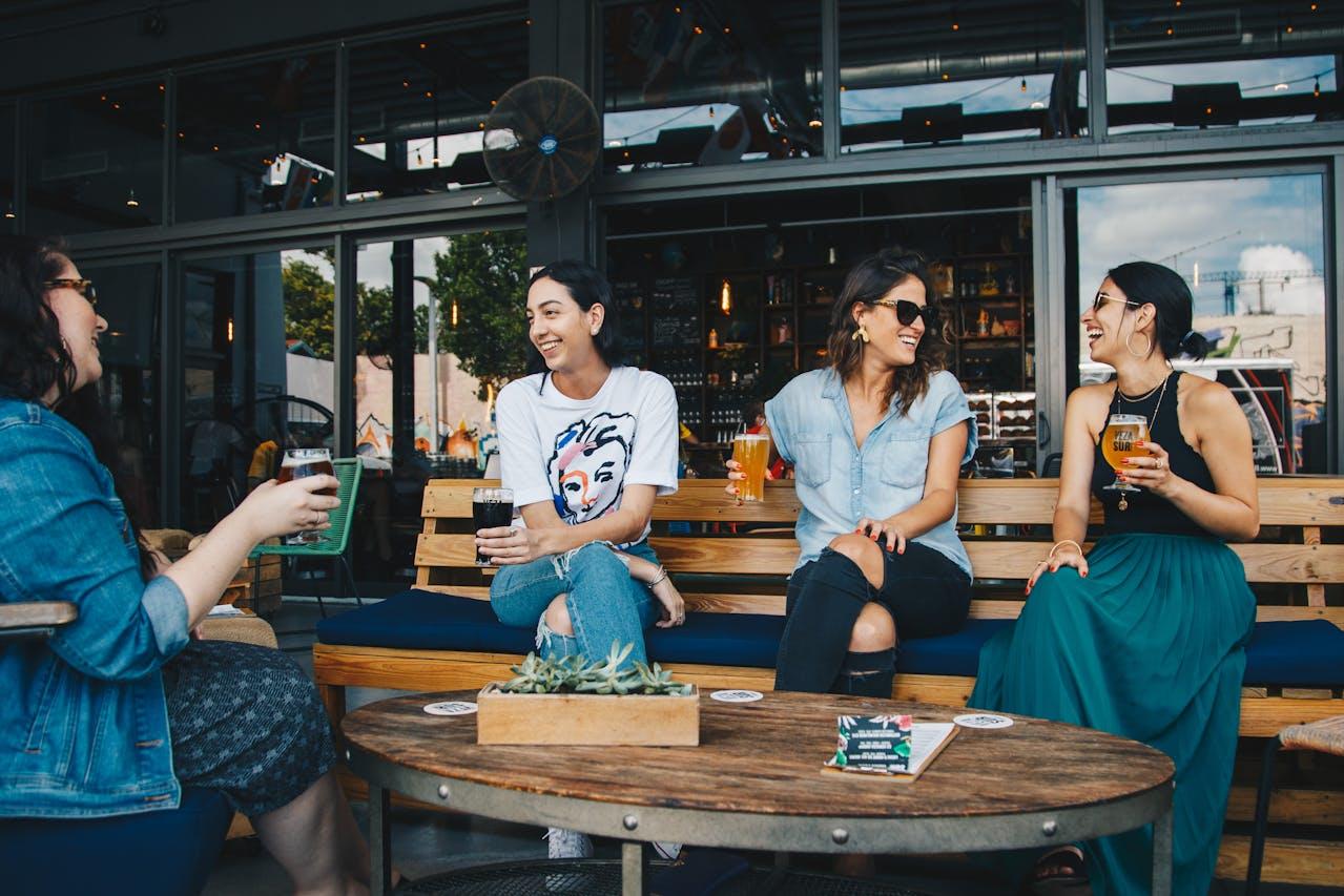 cuatro mujeres sentadas y sonrientes con un vaso de cerveza.