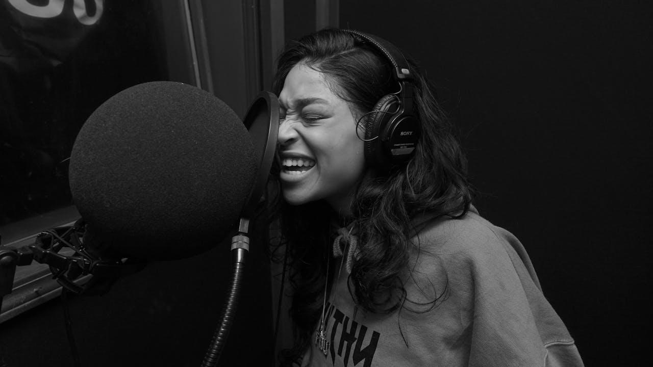 Mujer cantando frente al micrófono con auriculares.