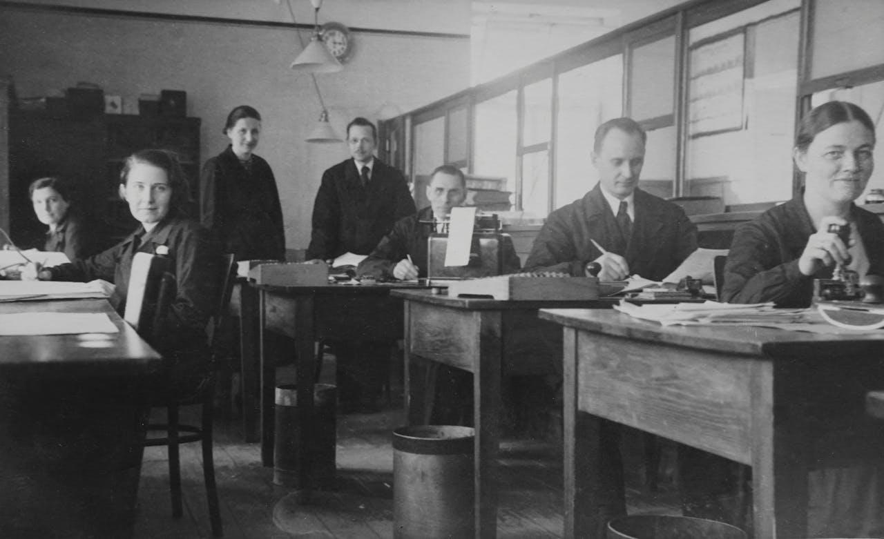 Mujeres y hombres sentados en escritorios con delantal.