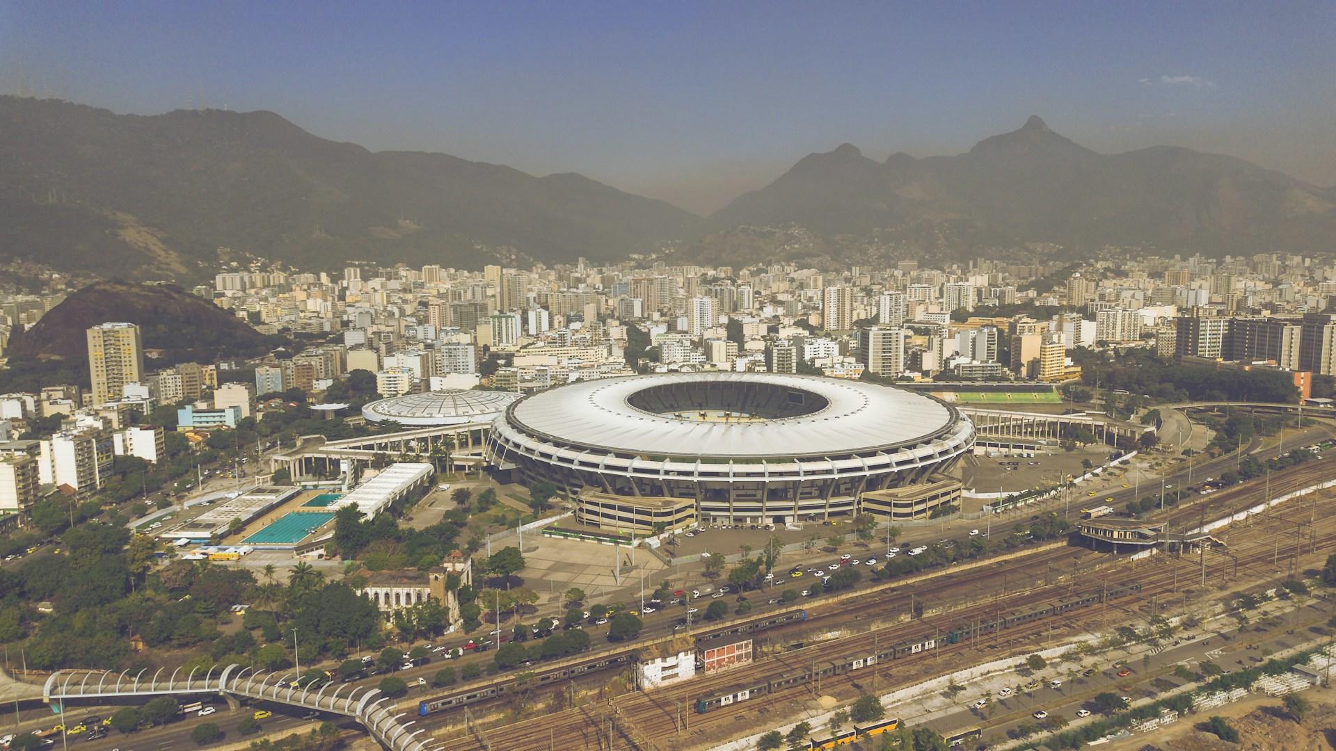 Estadio de fútbol rodeado de ciudad y montañas.