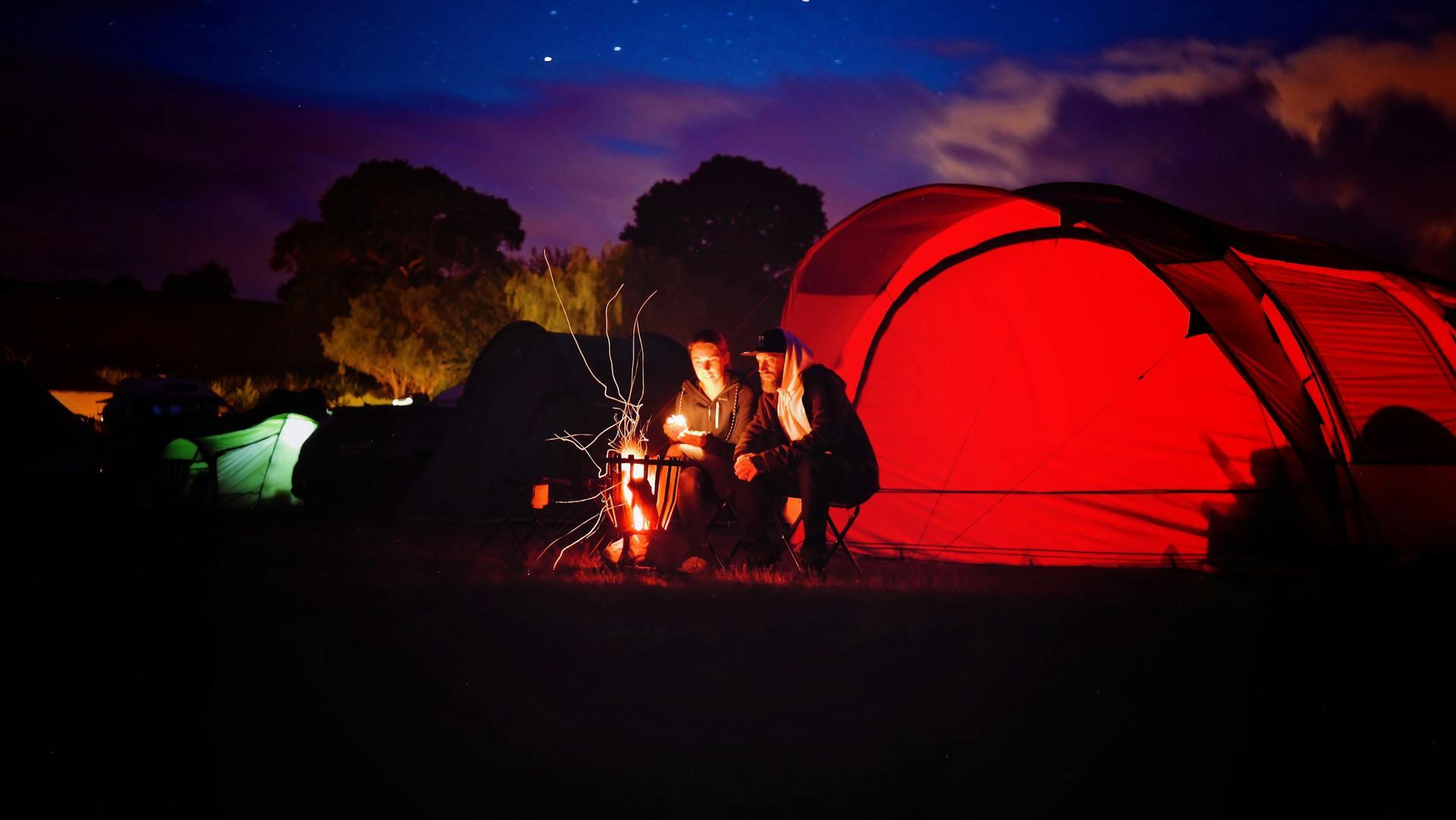 Dos personas sentados adelante de la carpa frente al fogón nocturno.