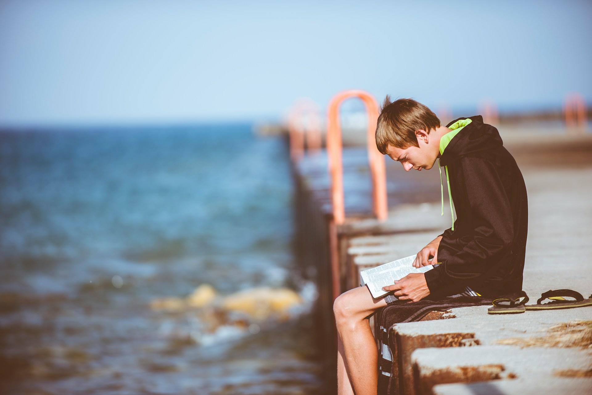 Niño leyendo sobre el muelle.