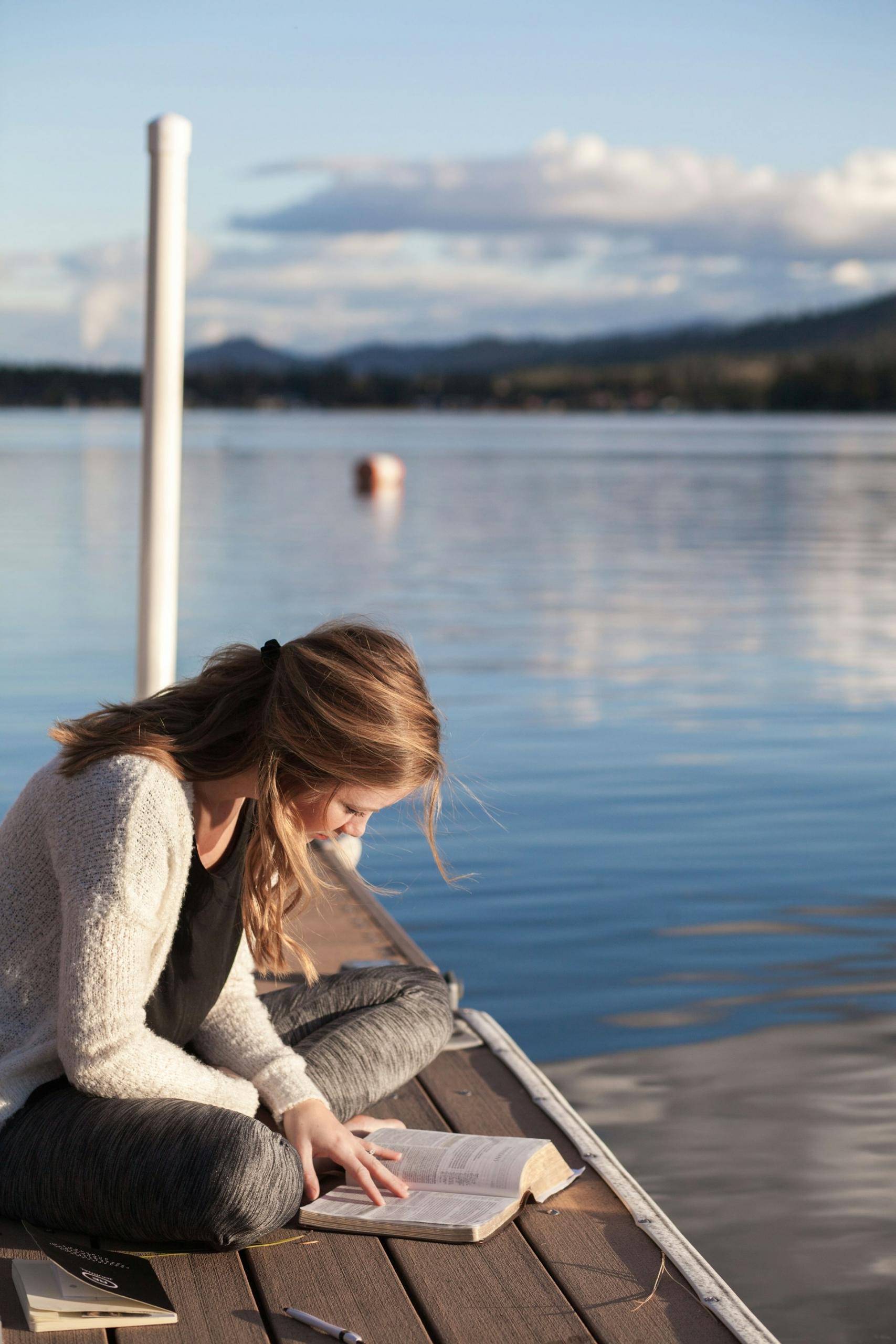 Mujer leyendo en el muelle de madera sobre el agua.