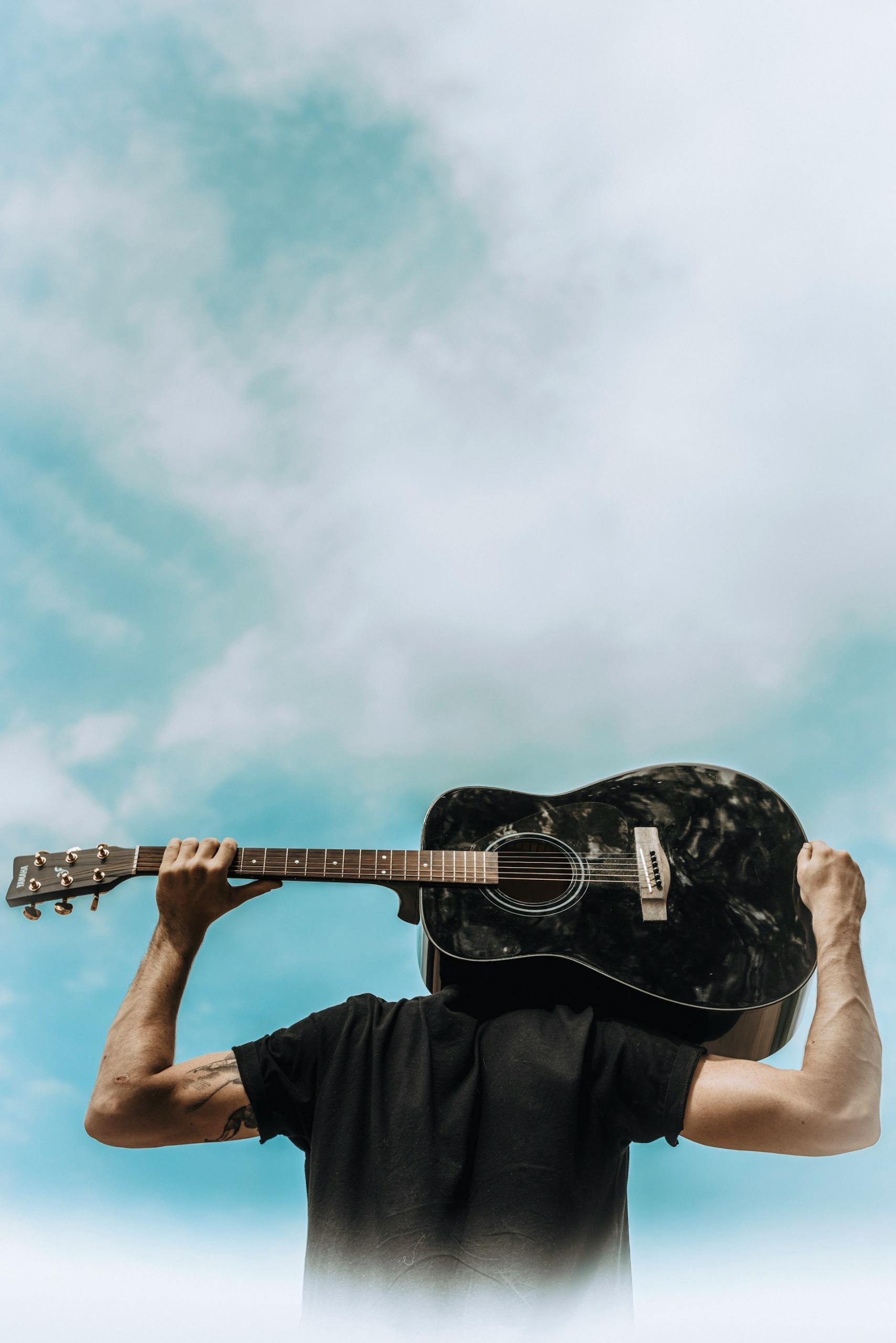 Hombre de espalda con una guitarra negra con cielo azul de fondo.