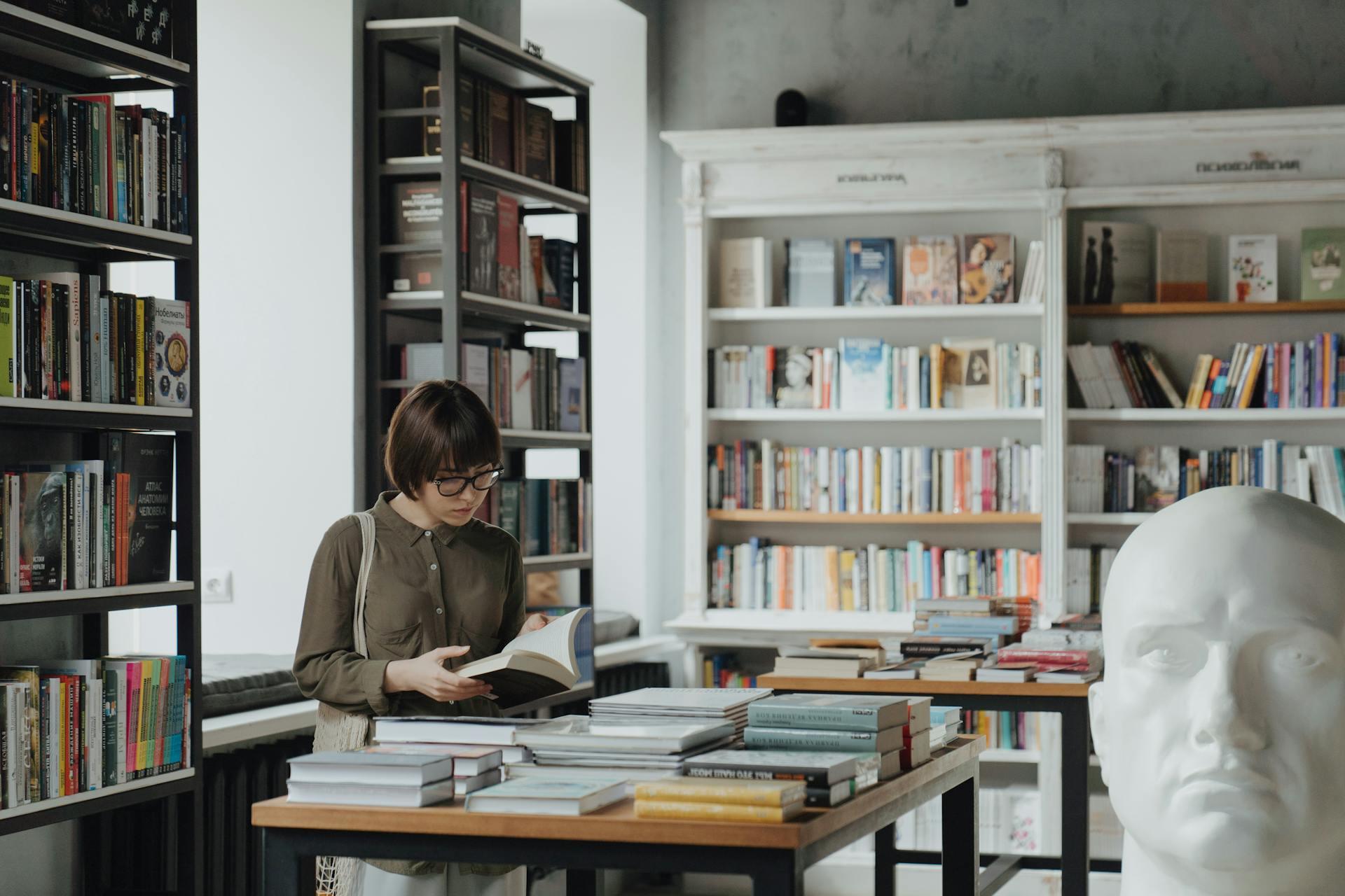 Mujer parada en la librería leyendo un libro.