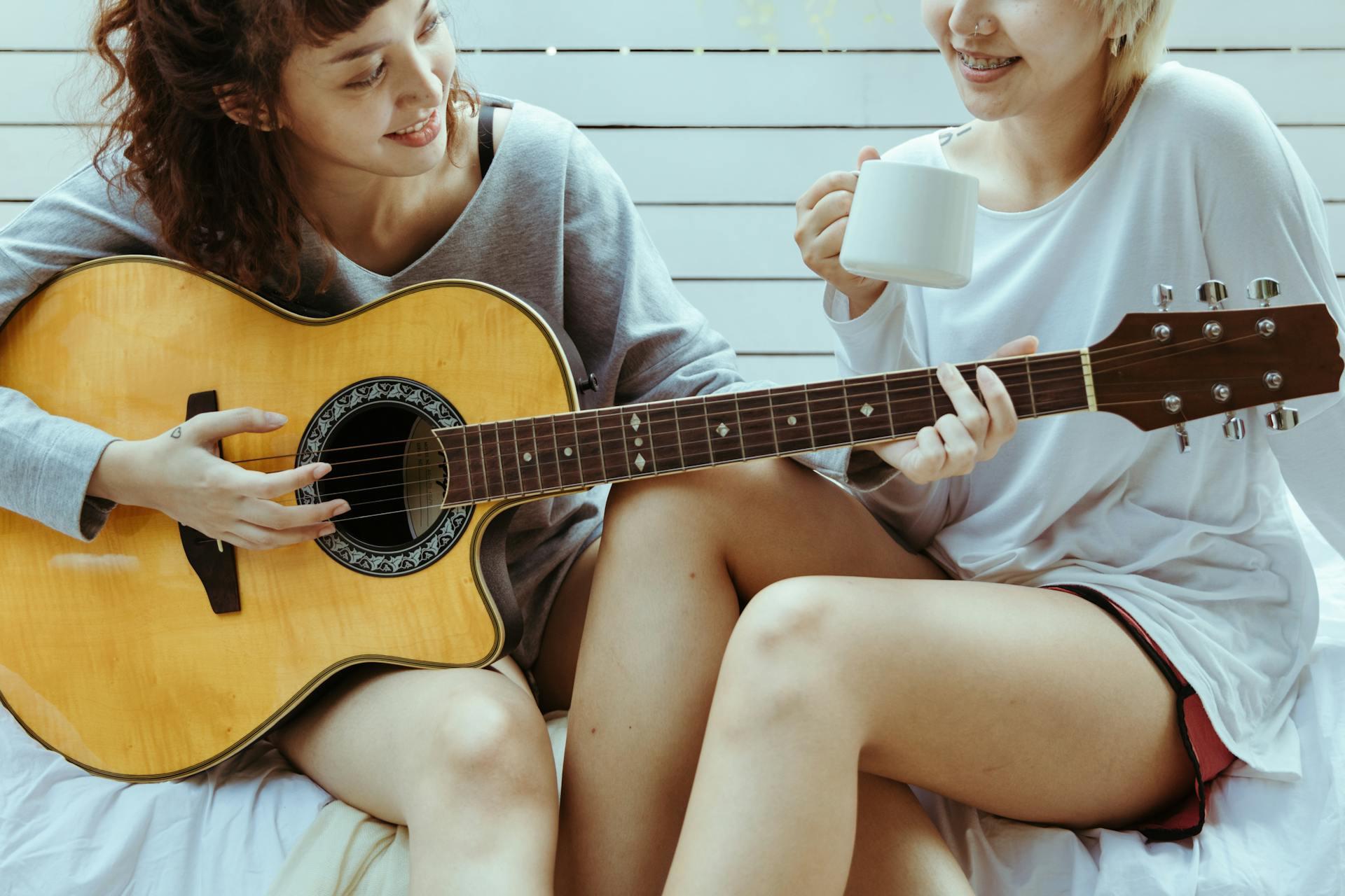 Dos mujeres tocando la guitarra sentadas en la cama.