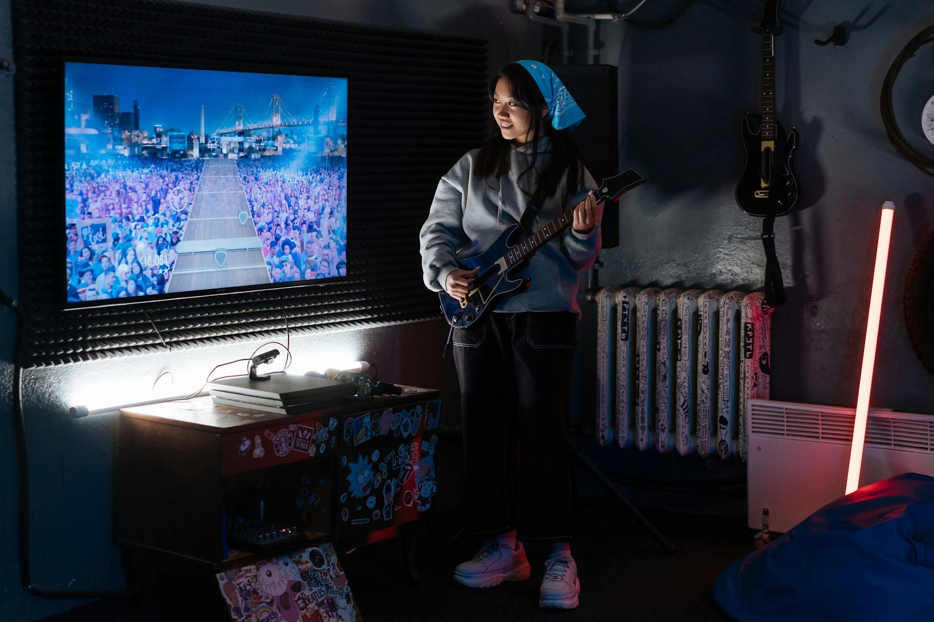 Mujer con una guitarra parada delante de la pantalla de la TV.