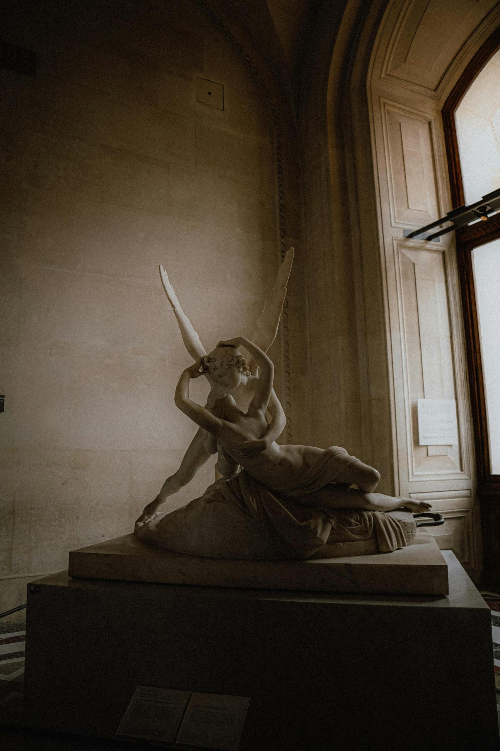 Escultura de piedra de un ángel tomando a una mujer desnuda.