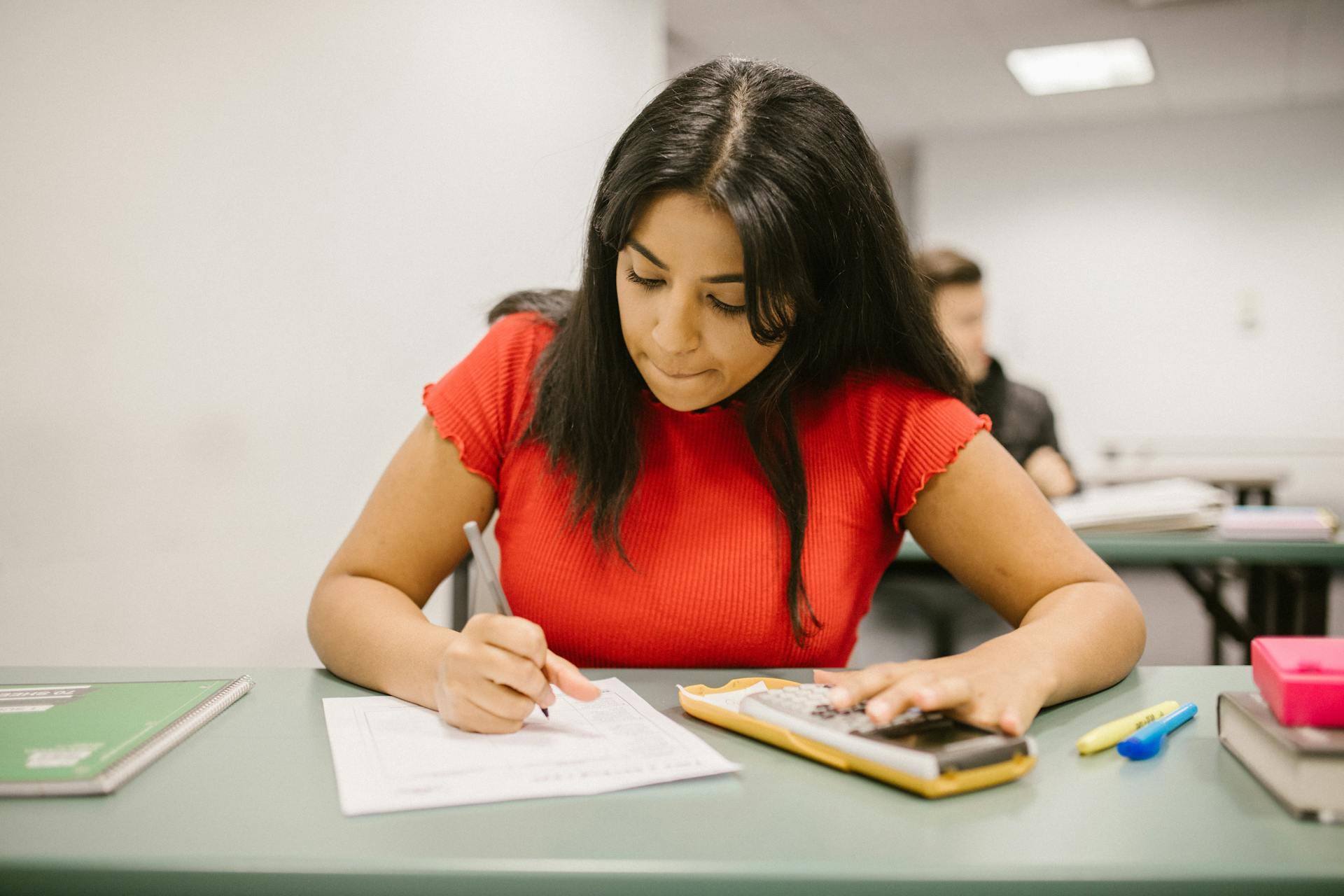 Mujer escribiendo con una calculadora en la mano.