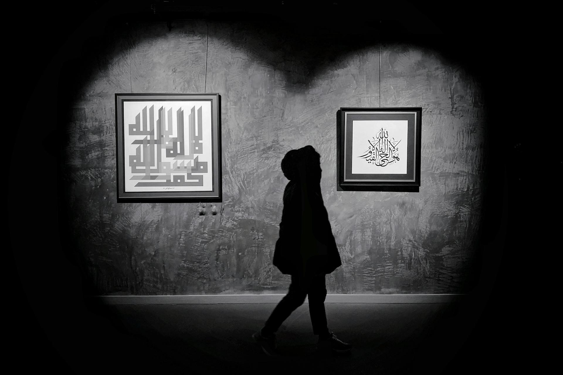 Foto blanco y negro de una persona con capucha mirando cuadros.