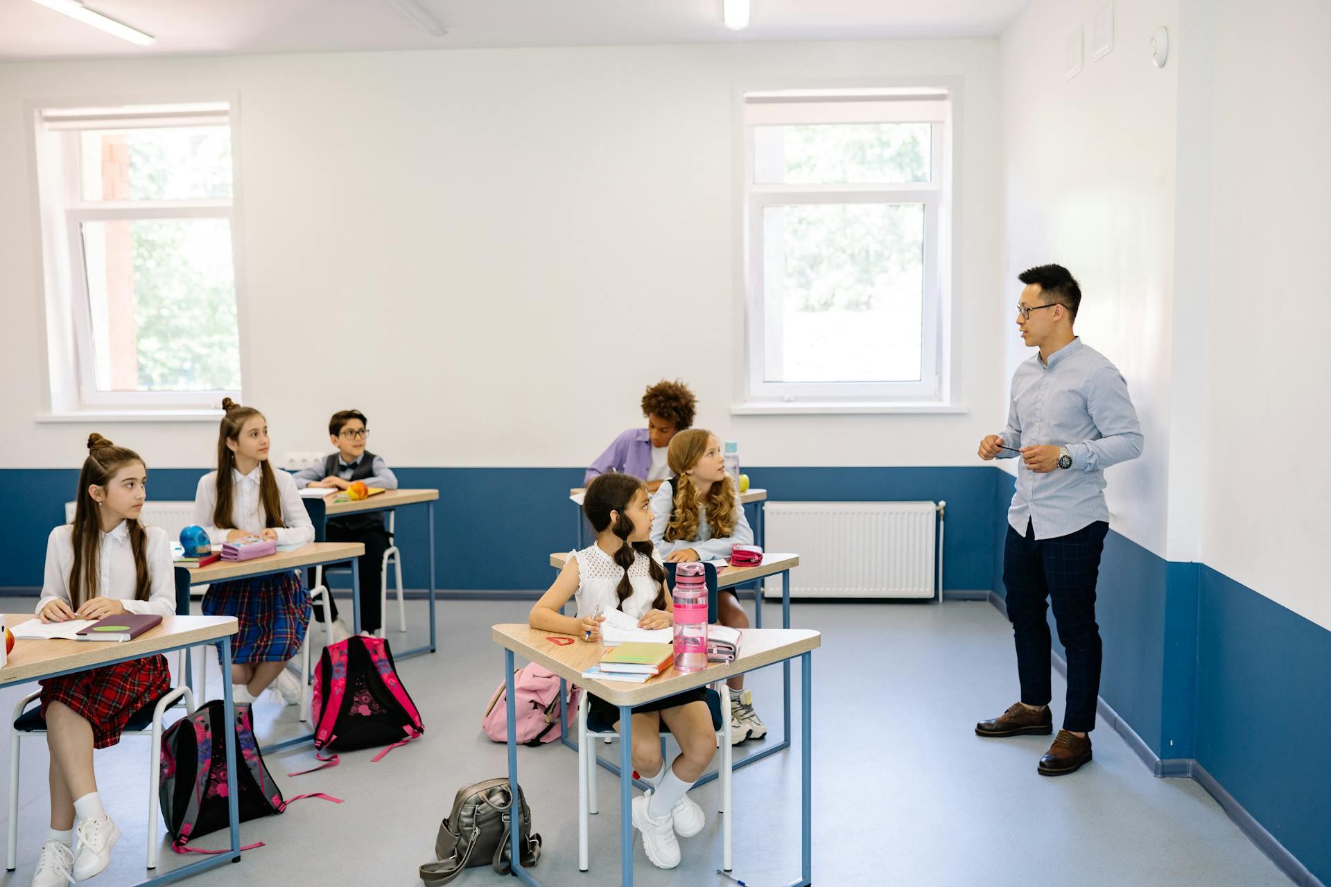 Niños sentados en pupitres dentro del aula azul y blanca.