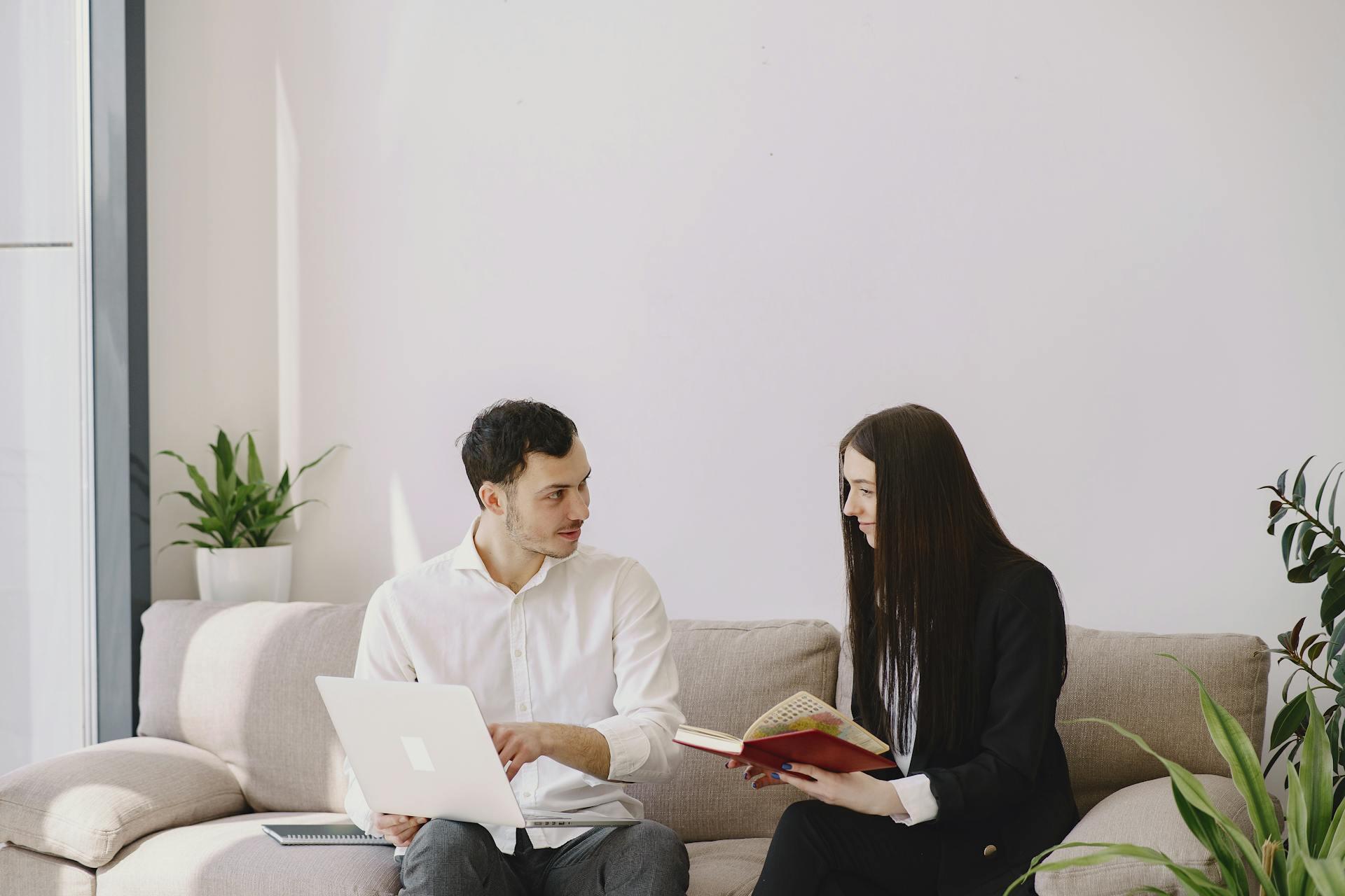 Un hombre y una mujer sentados en el sillón con una computadora y un libro.