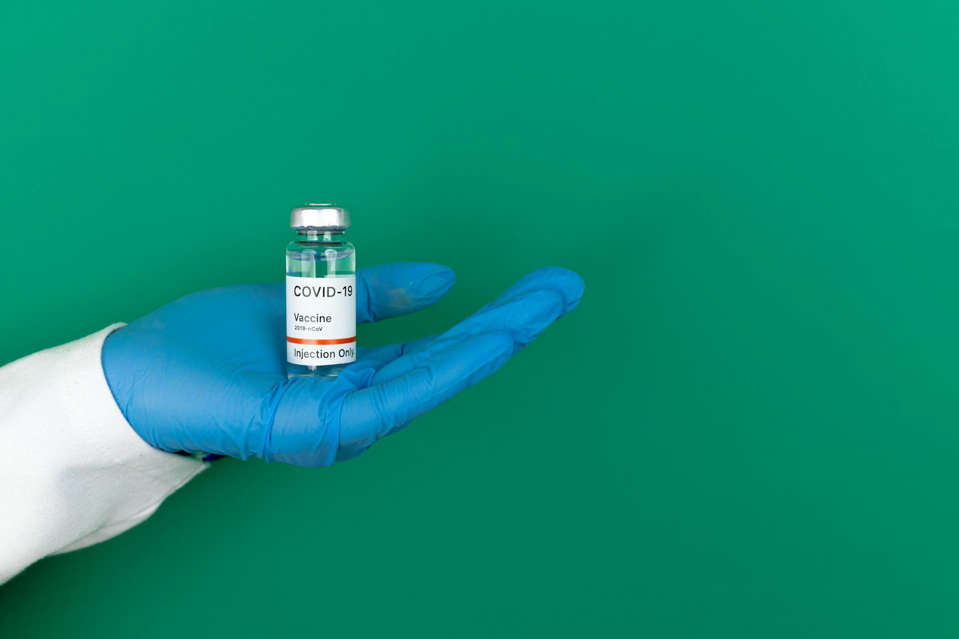 mano con guante de látex azul sosteniendo un frasco transparente con etiqueta blanca.