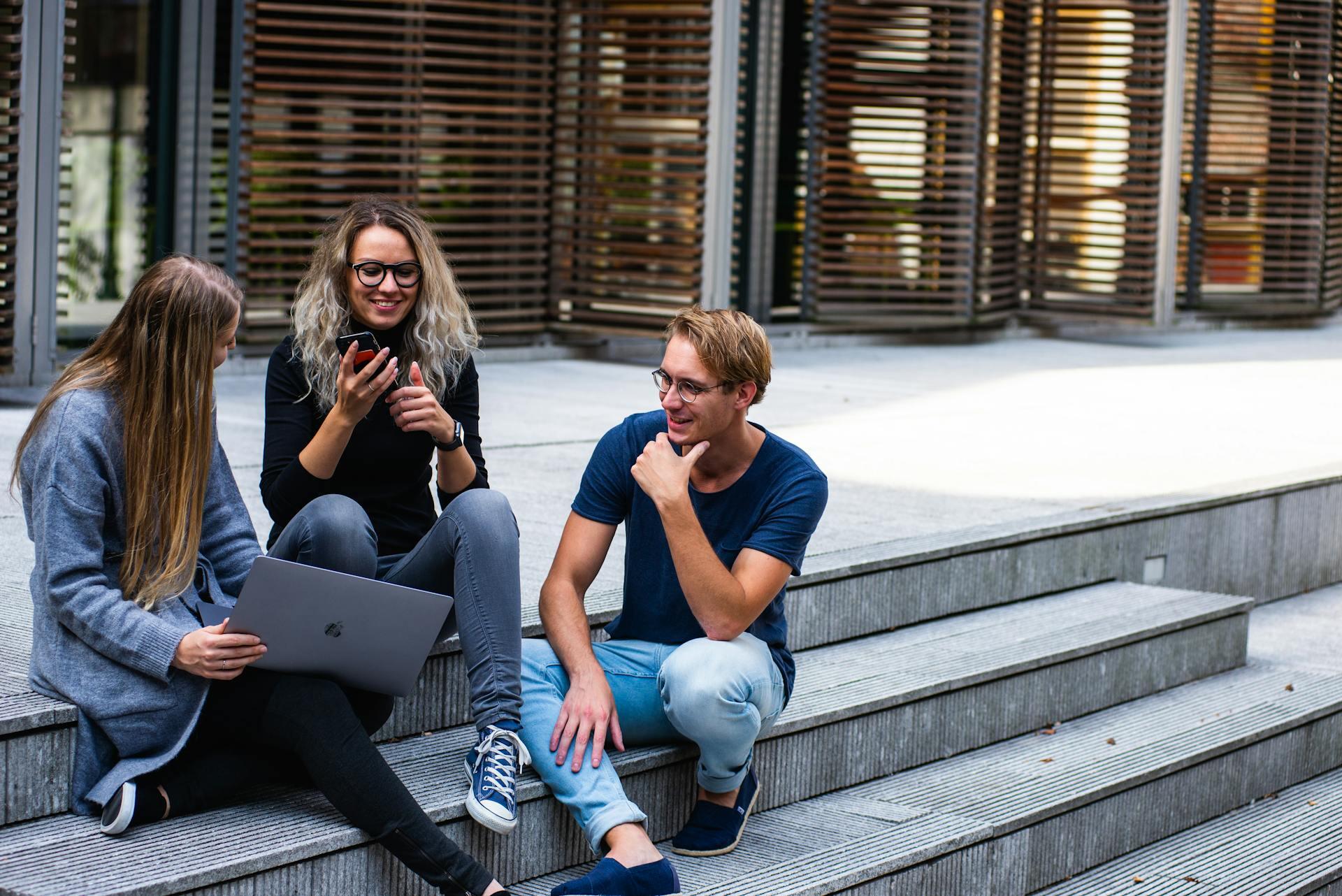 Tres jóvenes conversando sentados en las escaleras.
