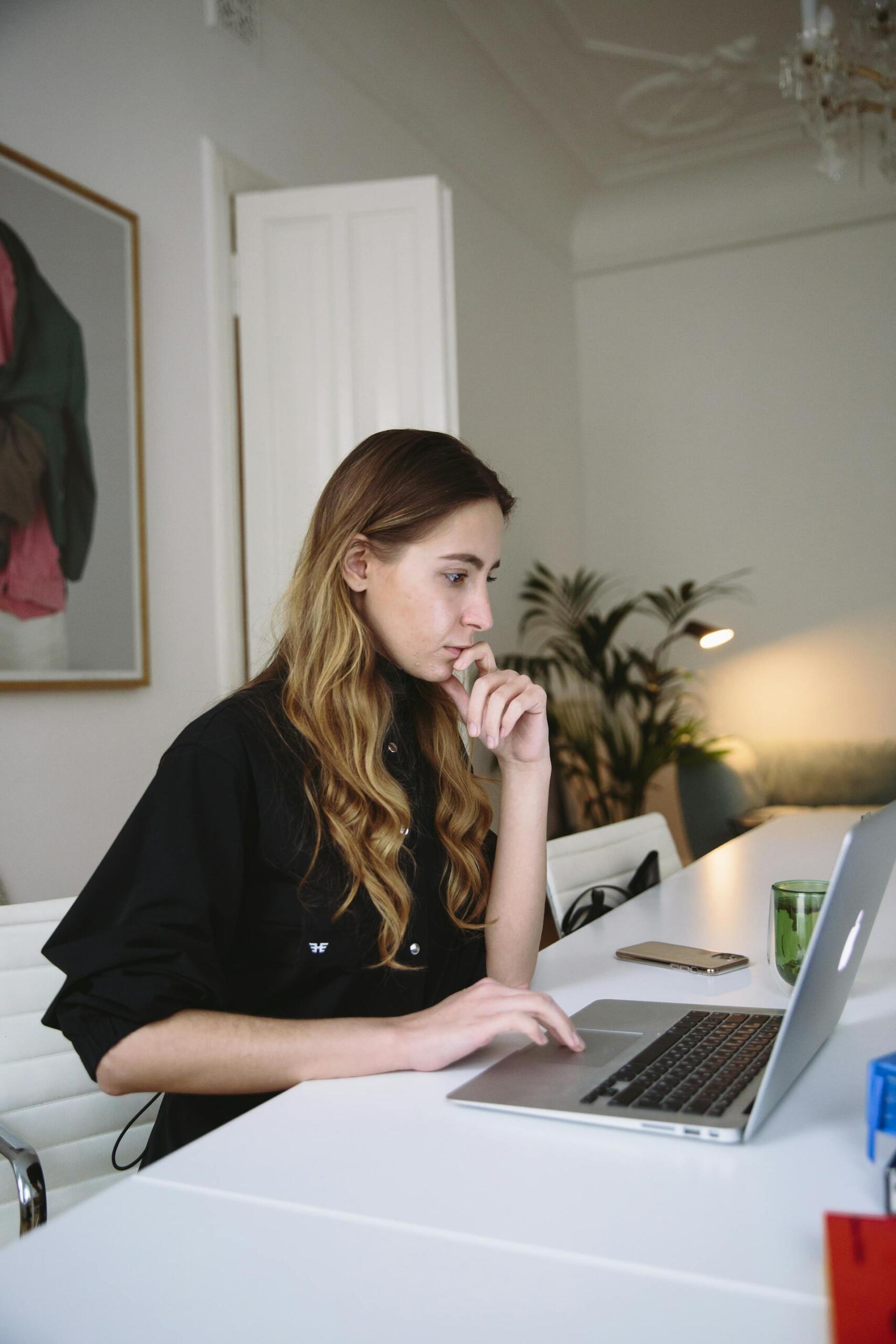 Mujer sentada en el escritorio blanco frente a la computadora.
