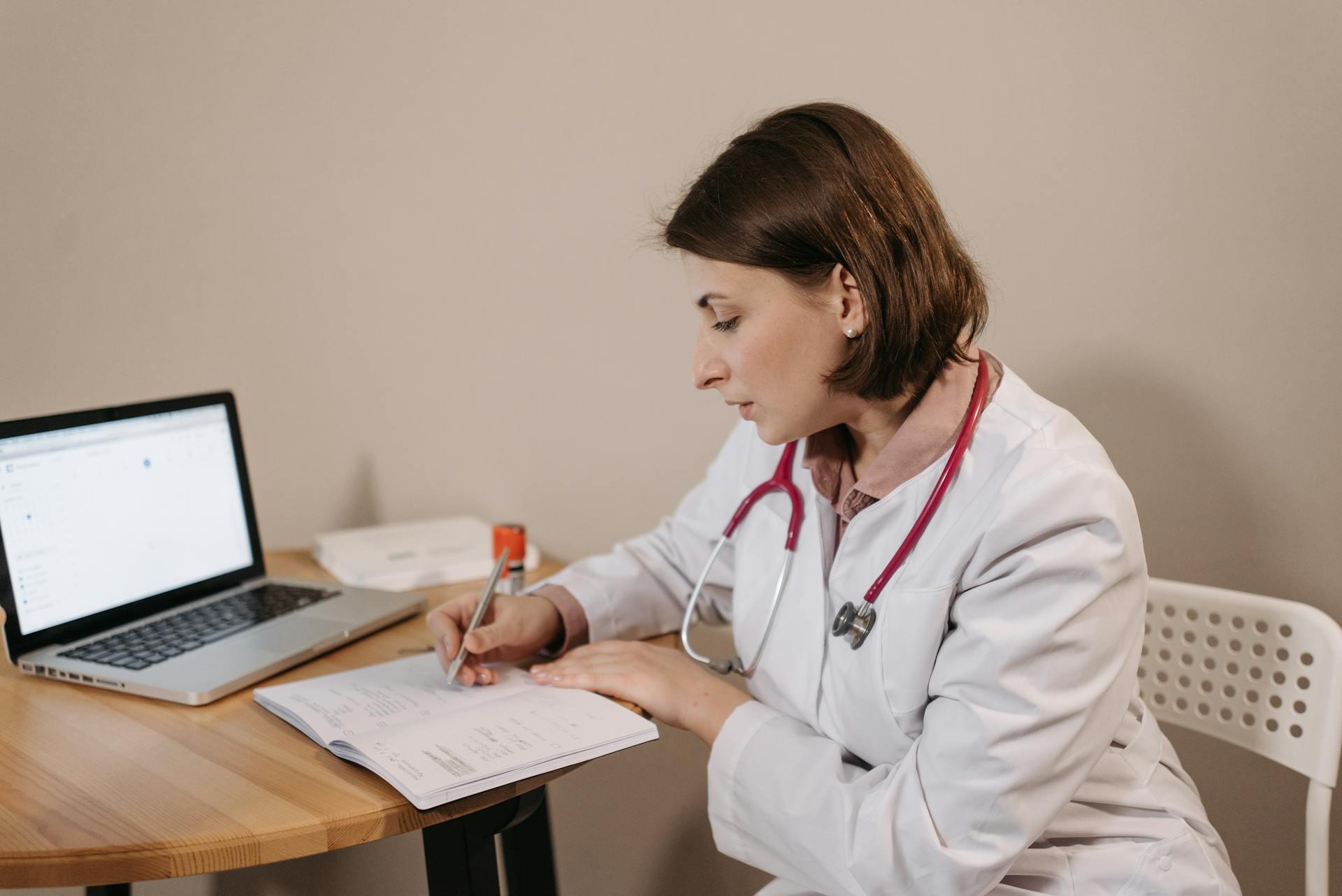 Mujer médica sentada en el escritorio escribiendo en el cuaderno.