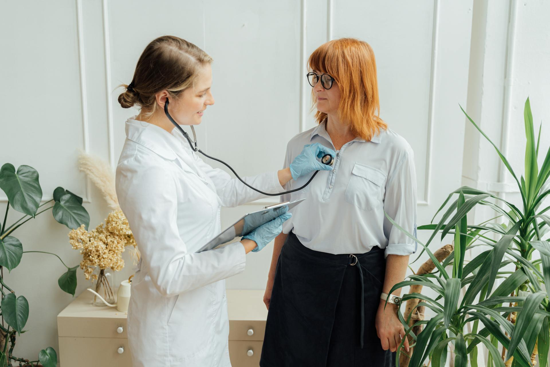 Médica con estetoscopio y cuaderno junto a la paciente.