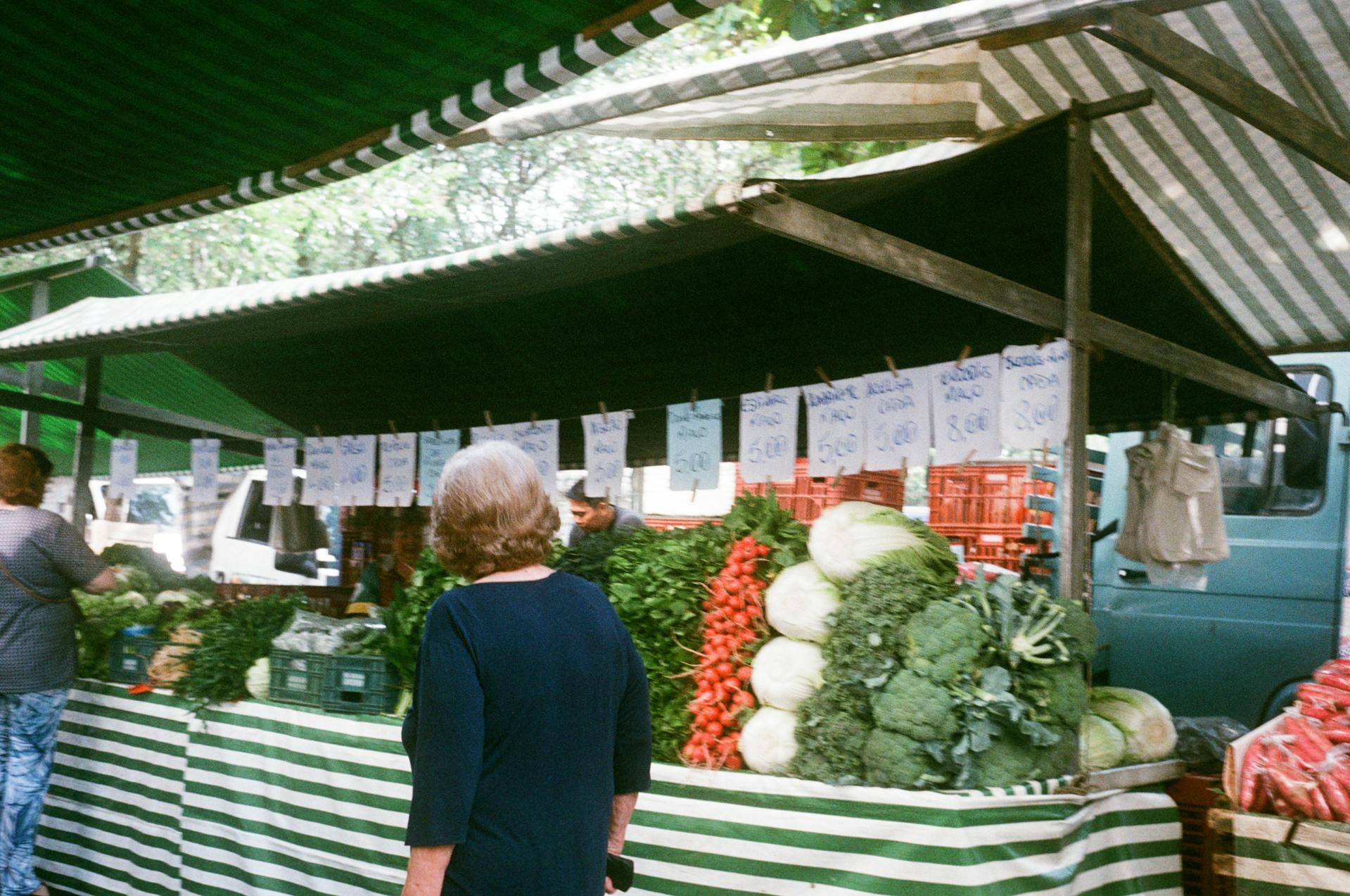 Mujer de espaldas mirando mercado de verduras.