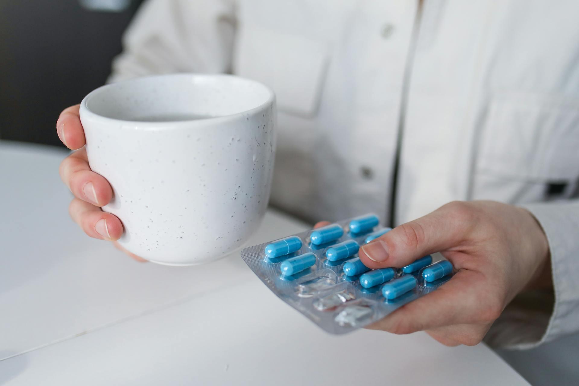 Persona con taza blanca y pastillas.