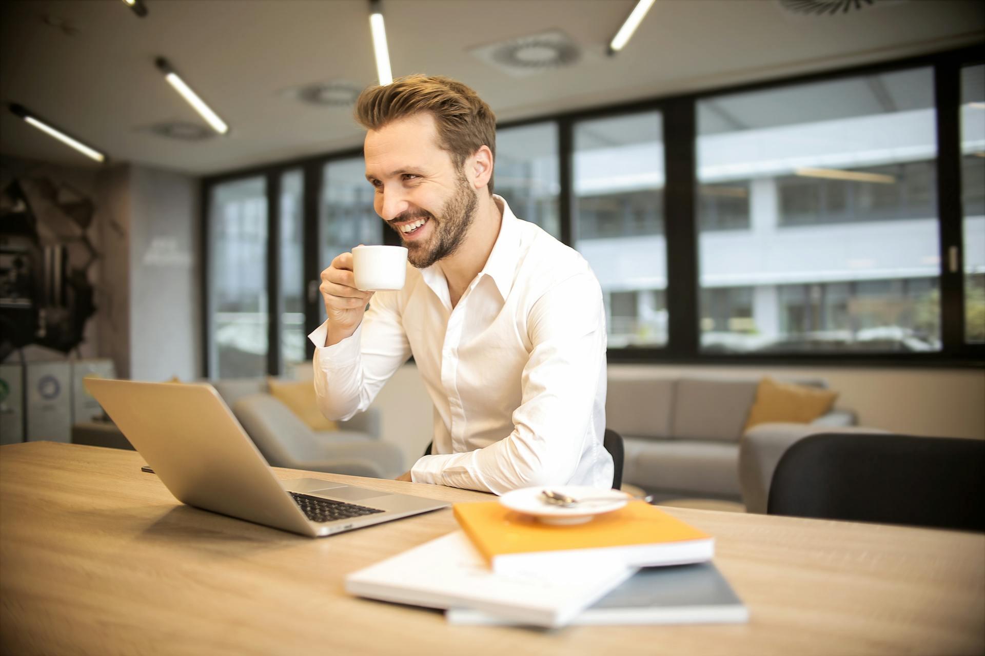 Hombre sentado en el escritorio frente a la PC con una taza de café en la mano.