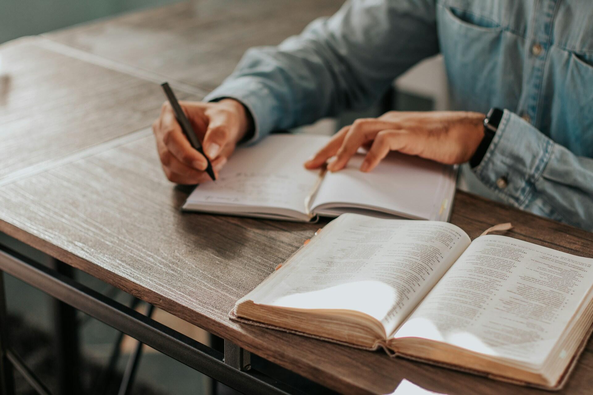 Persona con un libro abierto escribiendo en un cuaderno