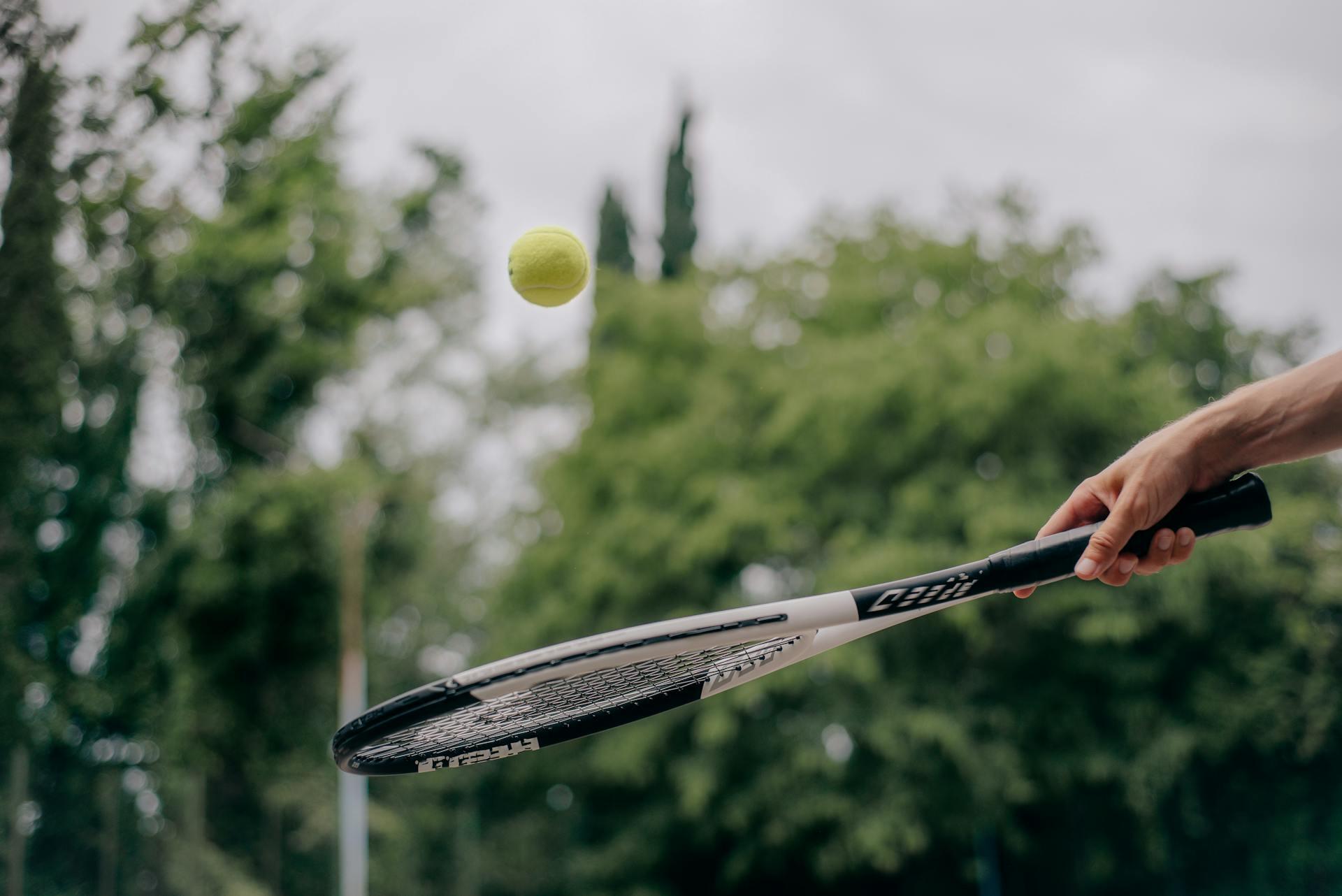 Mano sosteniendo una raqueta y pelota de tenis.