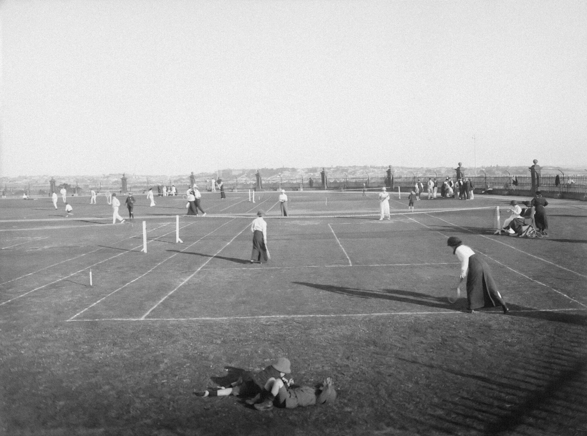 Cancha de tenis con jugadoras en blanco y negro.