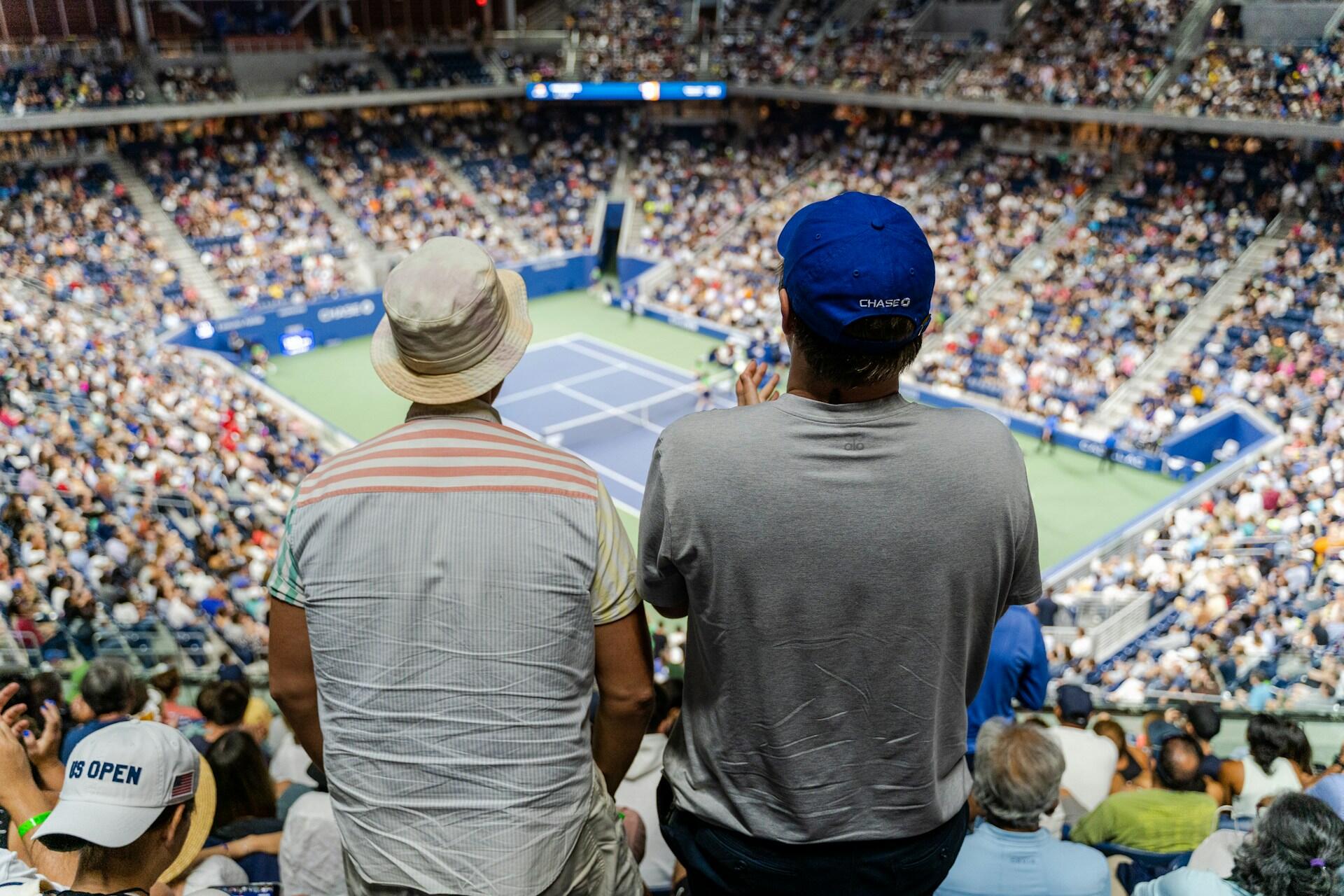 Dos hombres de espaldas mirando un partido de tenis. 