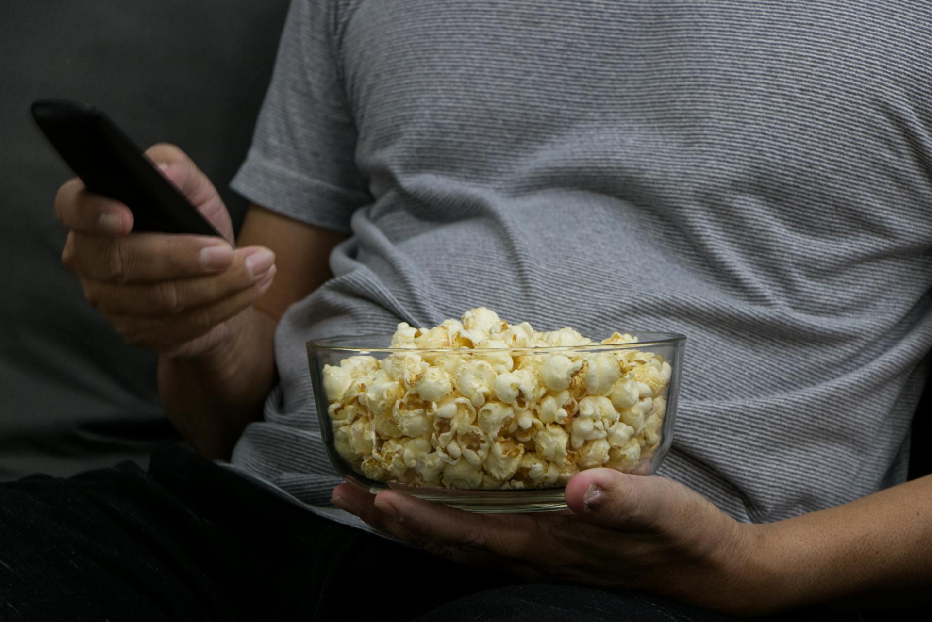 Hombre sosteniendo un bowl de pochoclos y control remoto. 