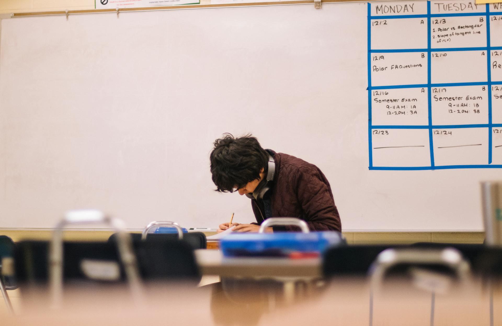 Alumno escribiendo sentado frente al pizarrón. 