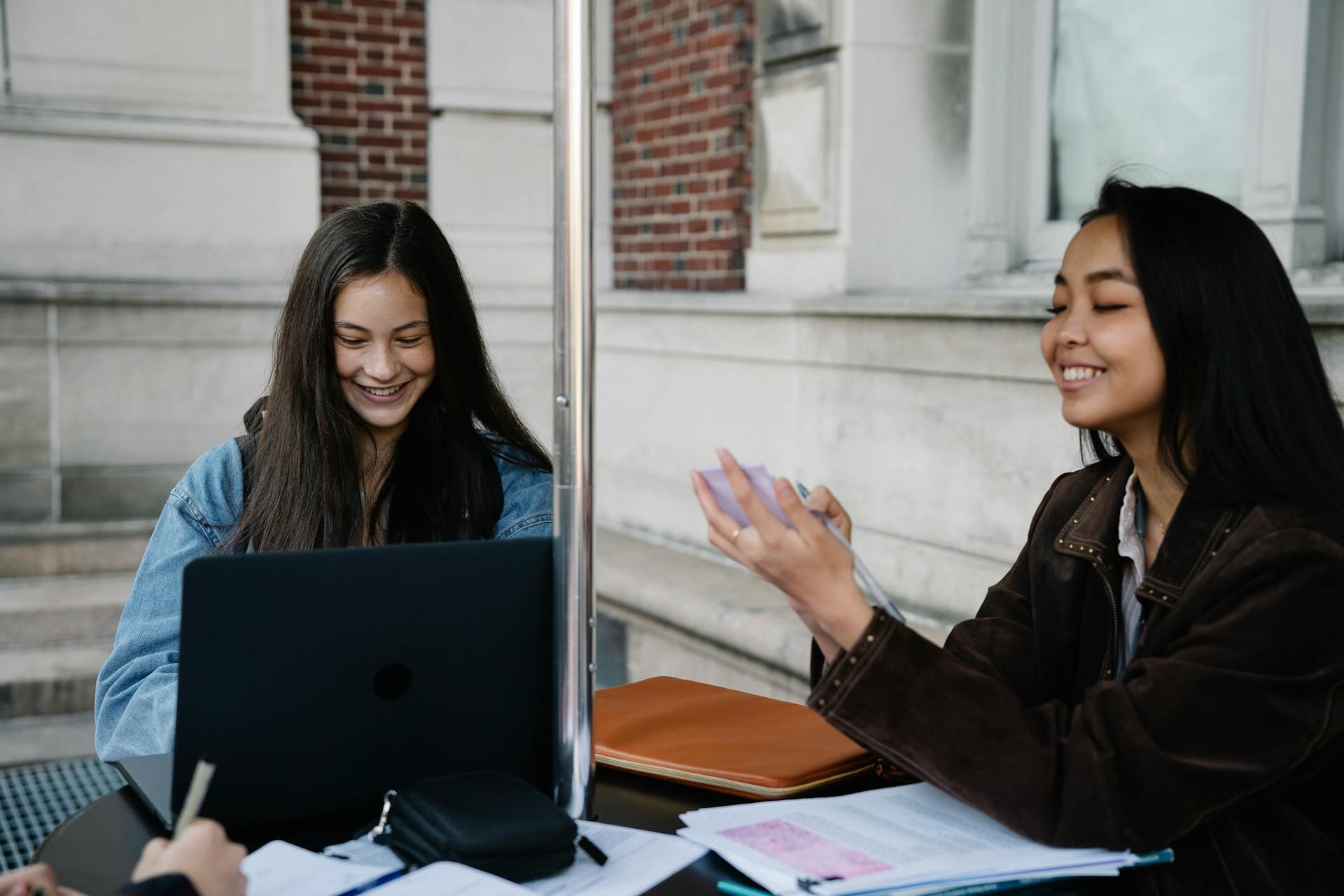 Dos mujeres sentadas en la mesa con papeles y PC. 