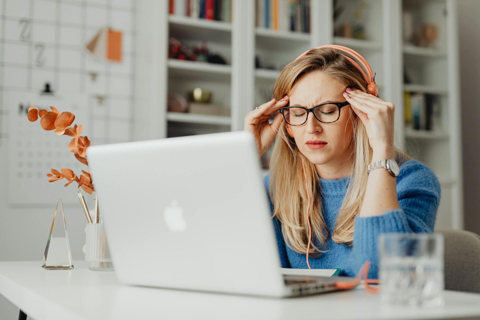 Mujer sentada frente a la pc con auriculares y los ojos cerrados. 