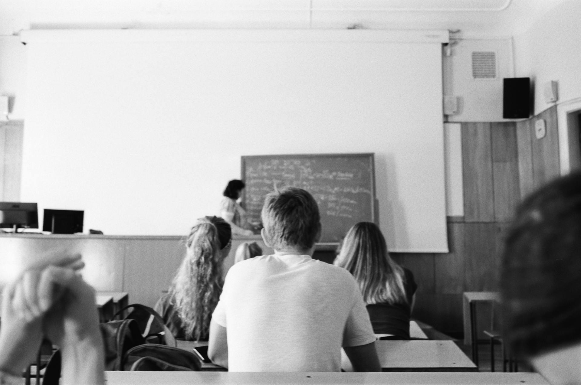 Foto en blanco y negro de alumnos en el aula escuchando a la profesora.