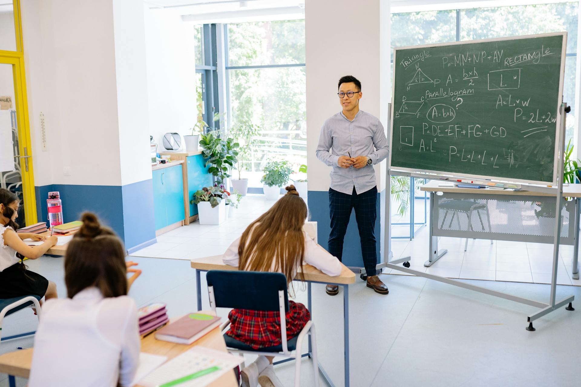 Profesor frente al pizarrón en el aula con alumnos.