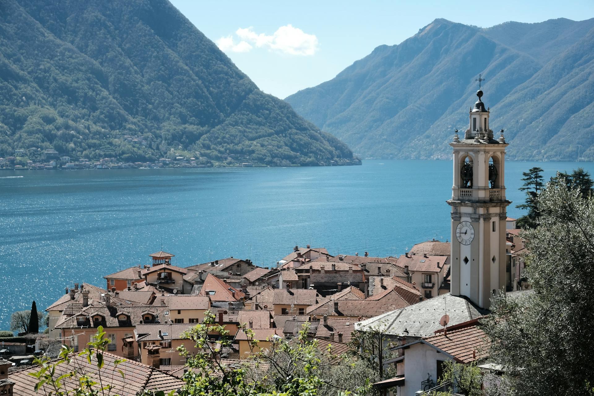 Paisaje de lago y montañas al lado de los tejados y de la cúpula de iglesia.