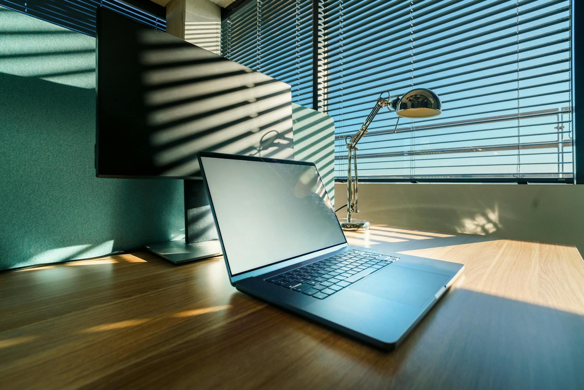 Escritorio de oficina moderno con portátil y monitor iluminados por el sol.