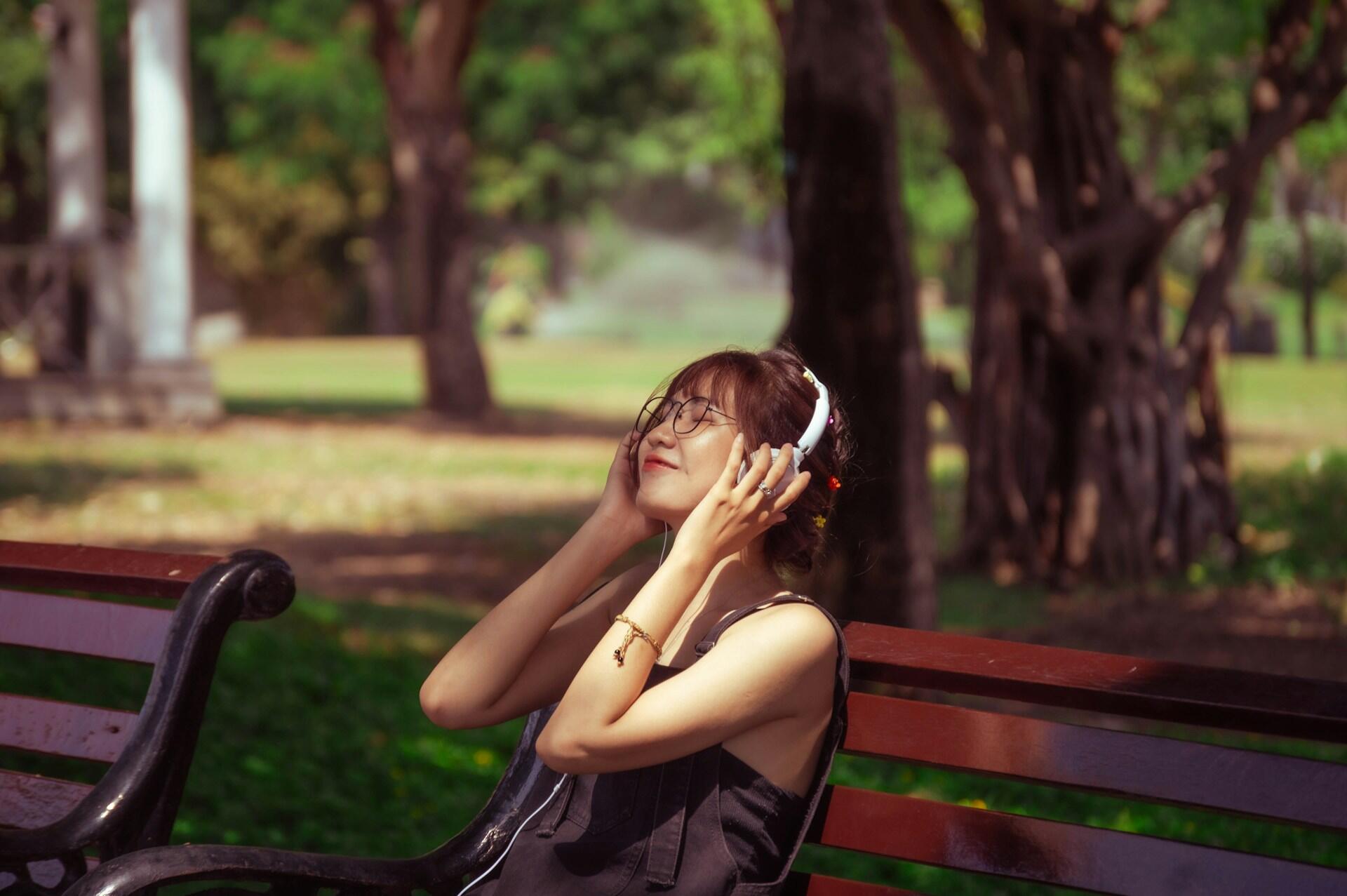 Mujer sentada en un banco de madera al aire libre con auriculares blancos.