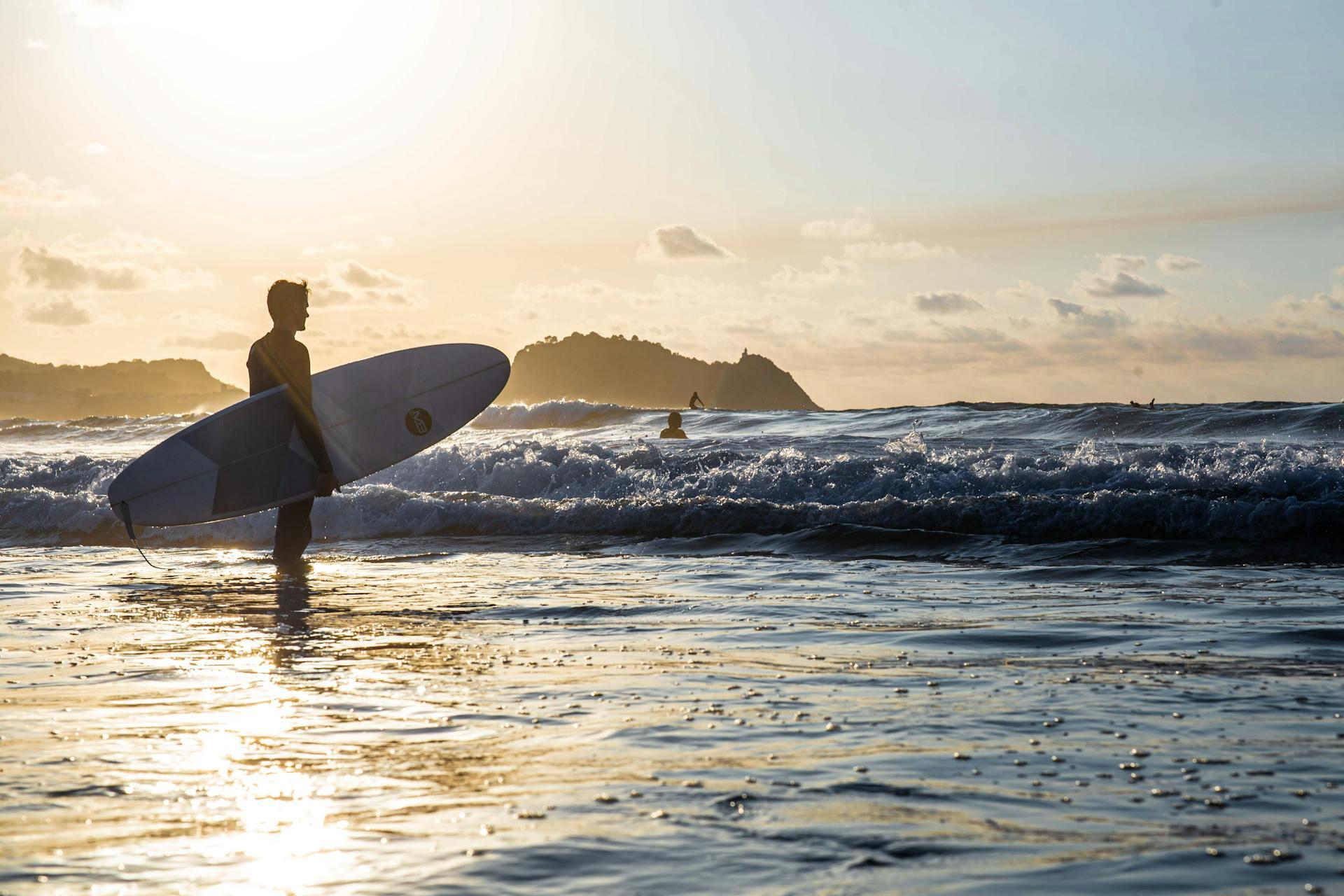Hombre parado en la orilla del mar sosteniendo una tabla de surf.