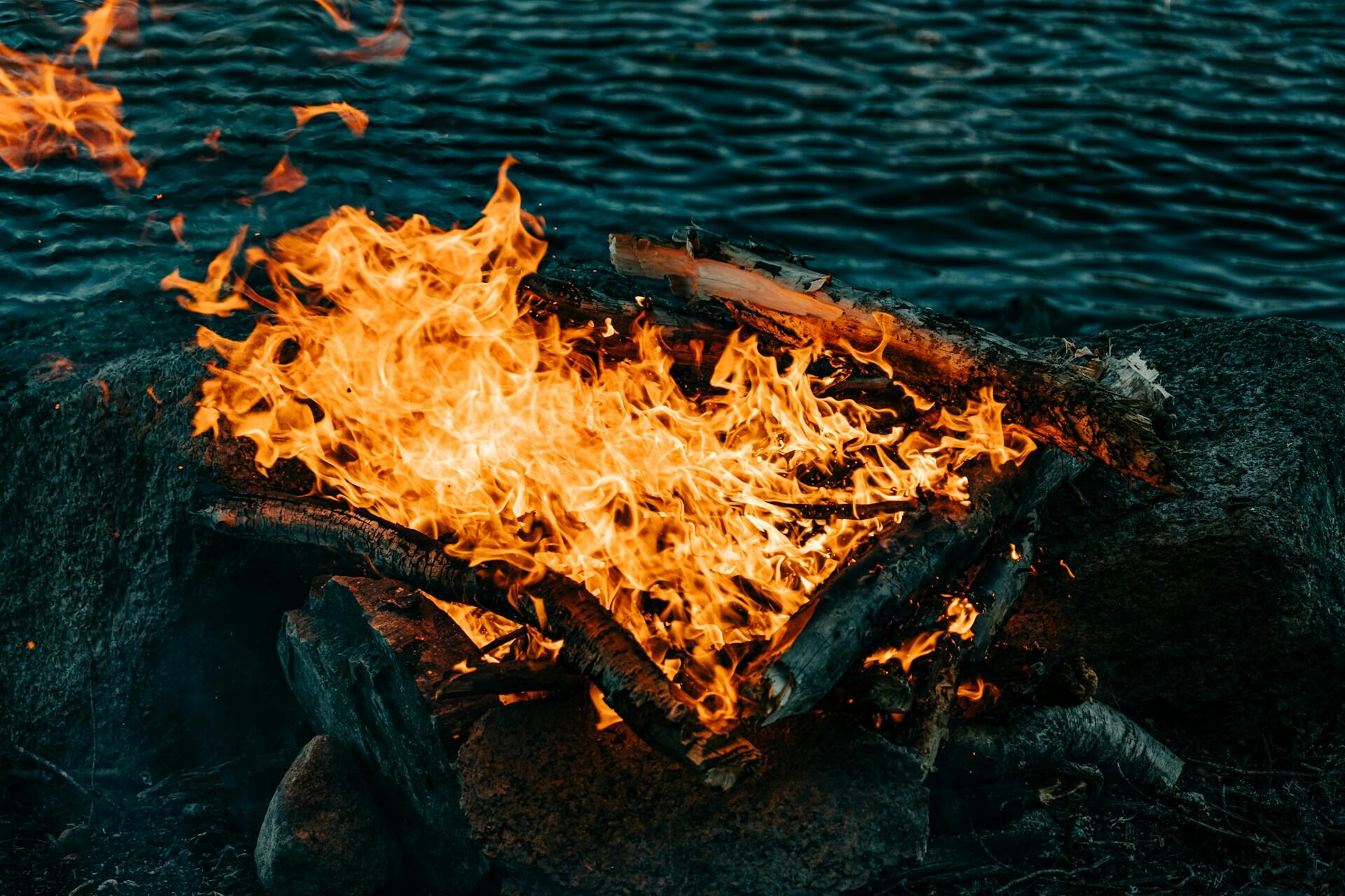 Primer plano de una hoguera ardiendo intensamente cerca del agua oscura, fotografía tomada por Niklas Håkonsen.