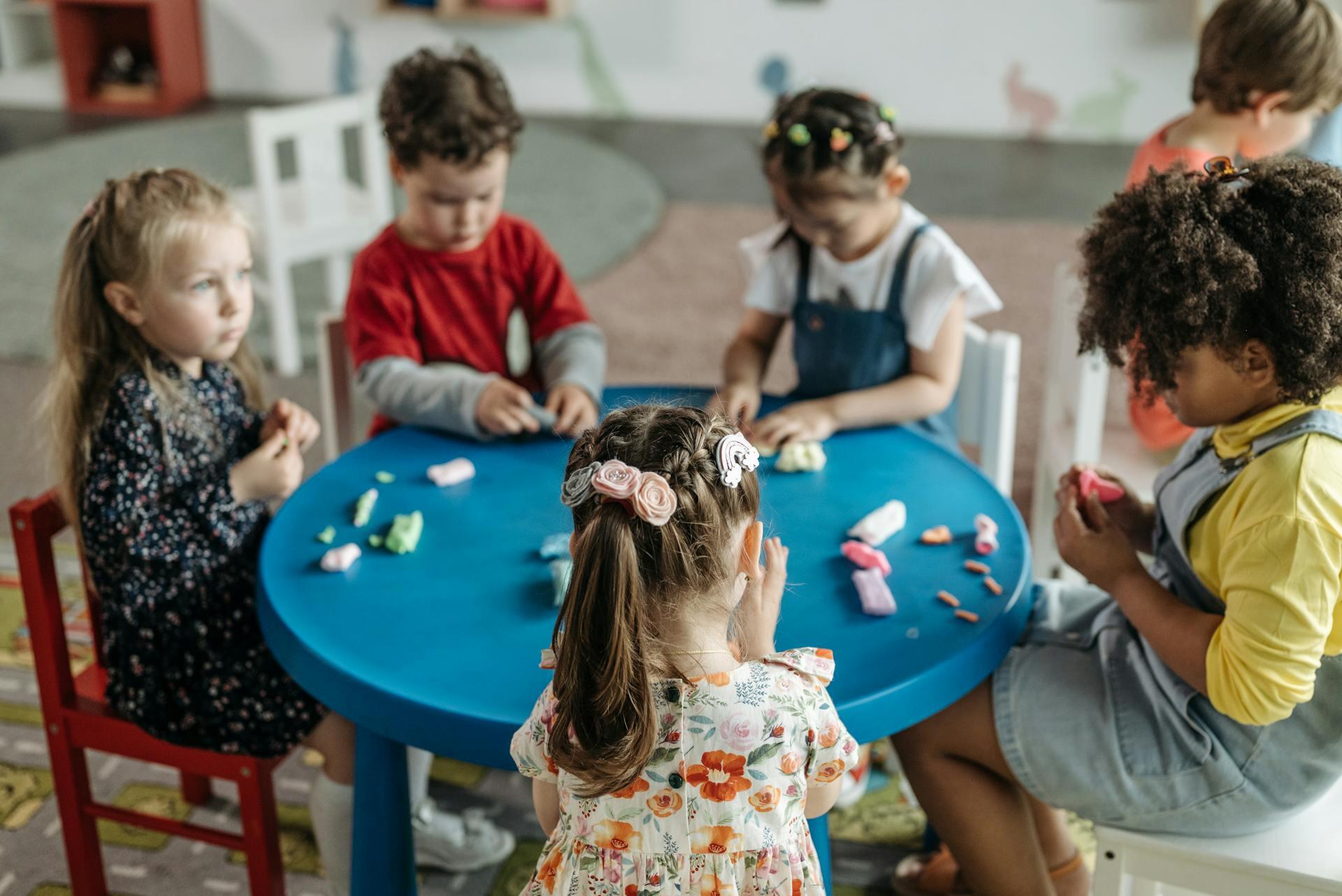 Niños sentados alrededor de la mesa redonda amasando plastilna.