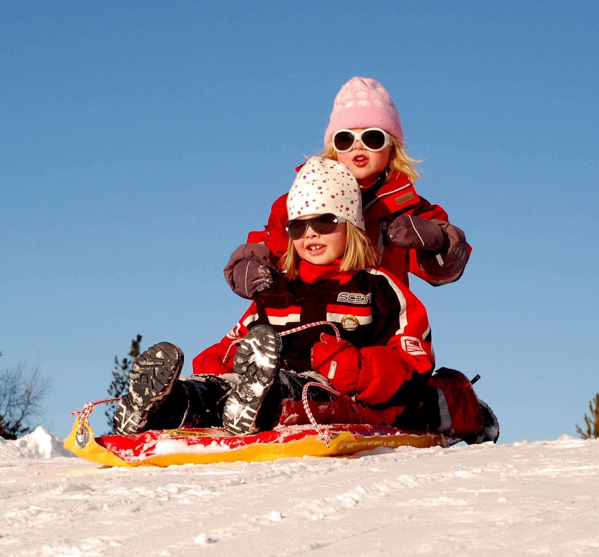 Niñas abrigadas sobre un trineo en la nieve.