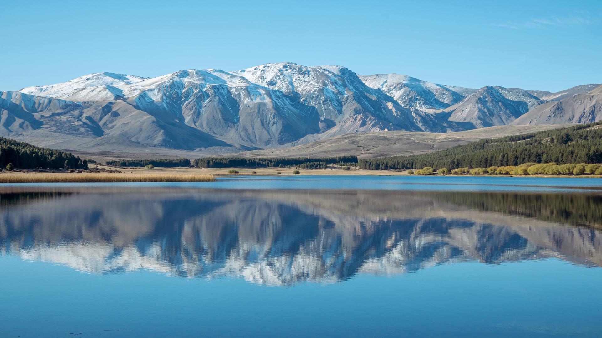 Paisaje de montañas nevadas y lago en Esquel, Chubut, representando la extensión del territorio argentino, por Ema Reynares.