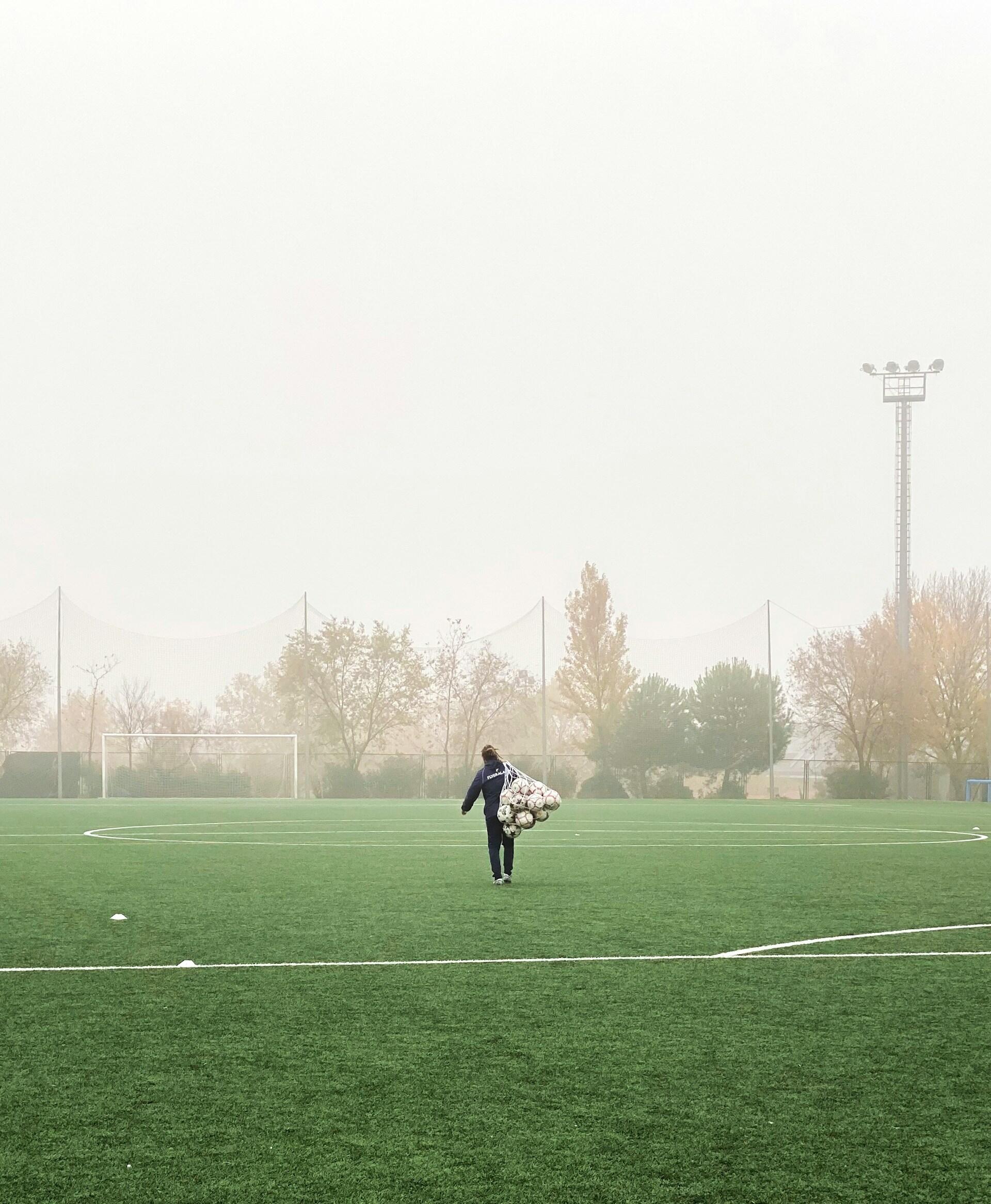Un campo de entrenamiento donde una persona carga una bolsa llena de pelotas de fútbol. Fuente: Alberto Frías.