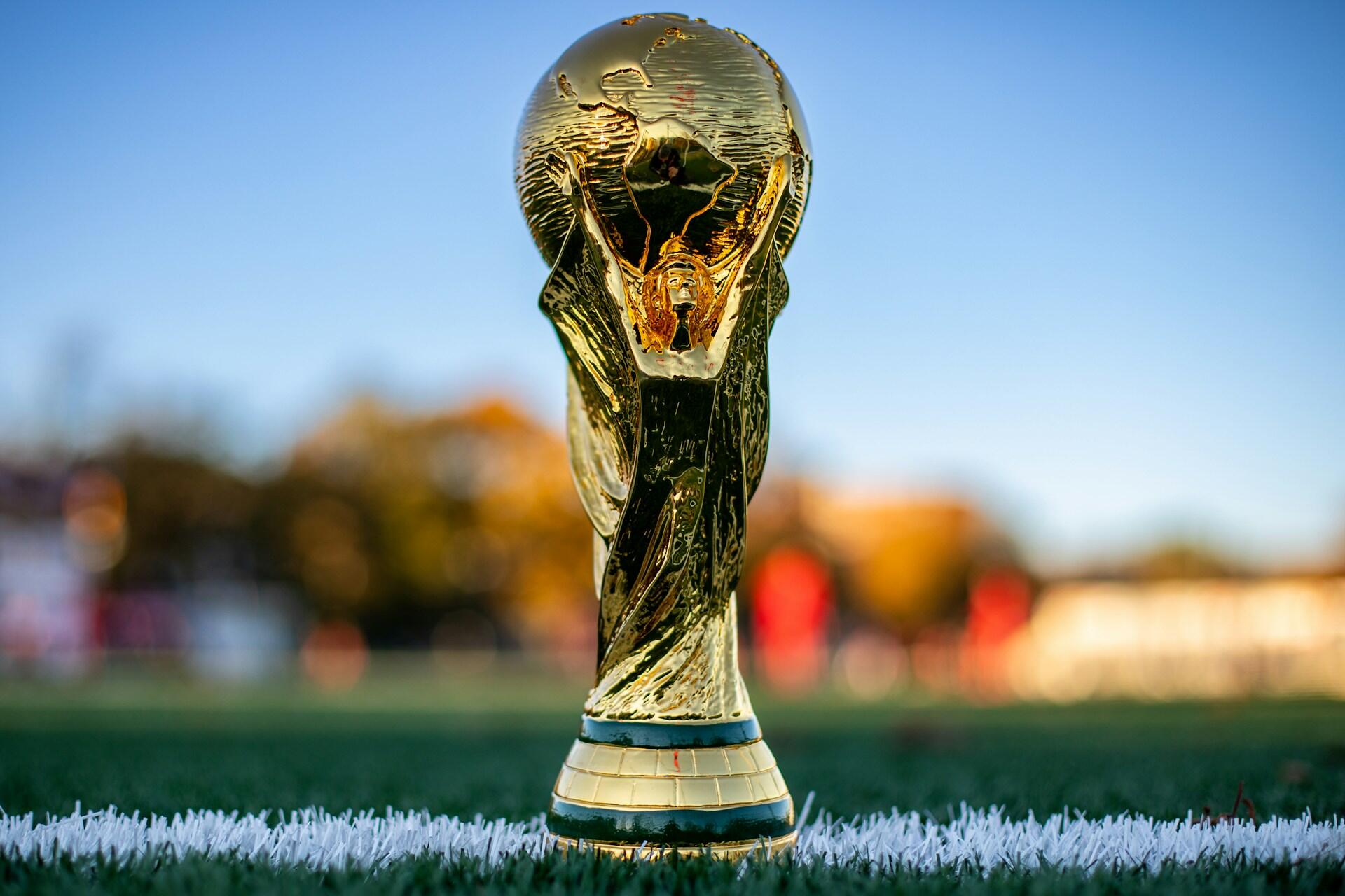 Unsplash: Trofeo de la Copa del Mundo de la FIFA sobre la línea blanca del césped de una cancha de fútbol, por My Profit Tutor.