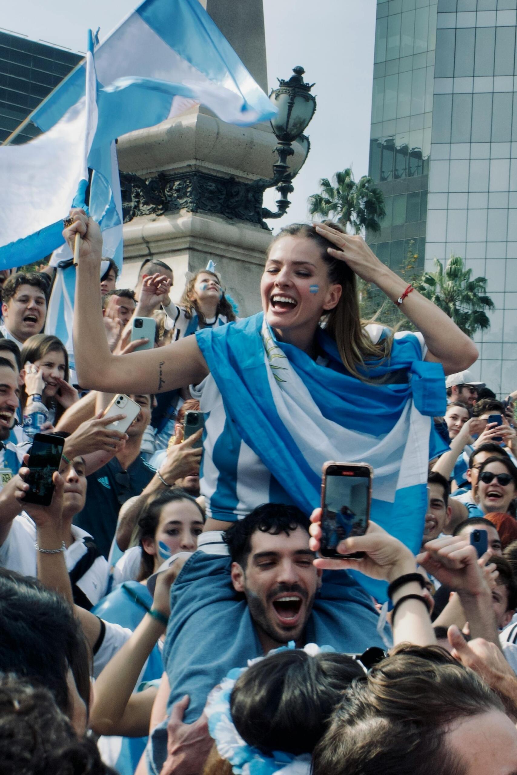 Buenos Aires, Argentina. Una hincha celebra con una bandera argentina sobre los hombros en medio de una multitud durante los festejos. Fotografía de Raul Albright.