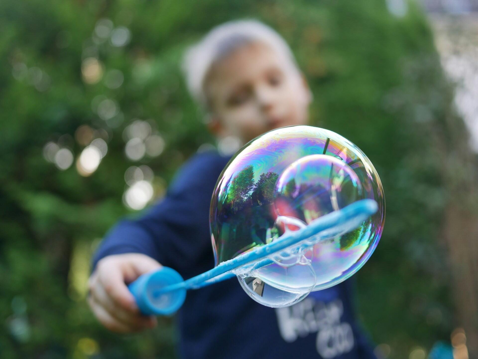 Niño sosteniendo un aro azul del que sale una burbuja.