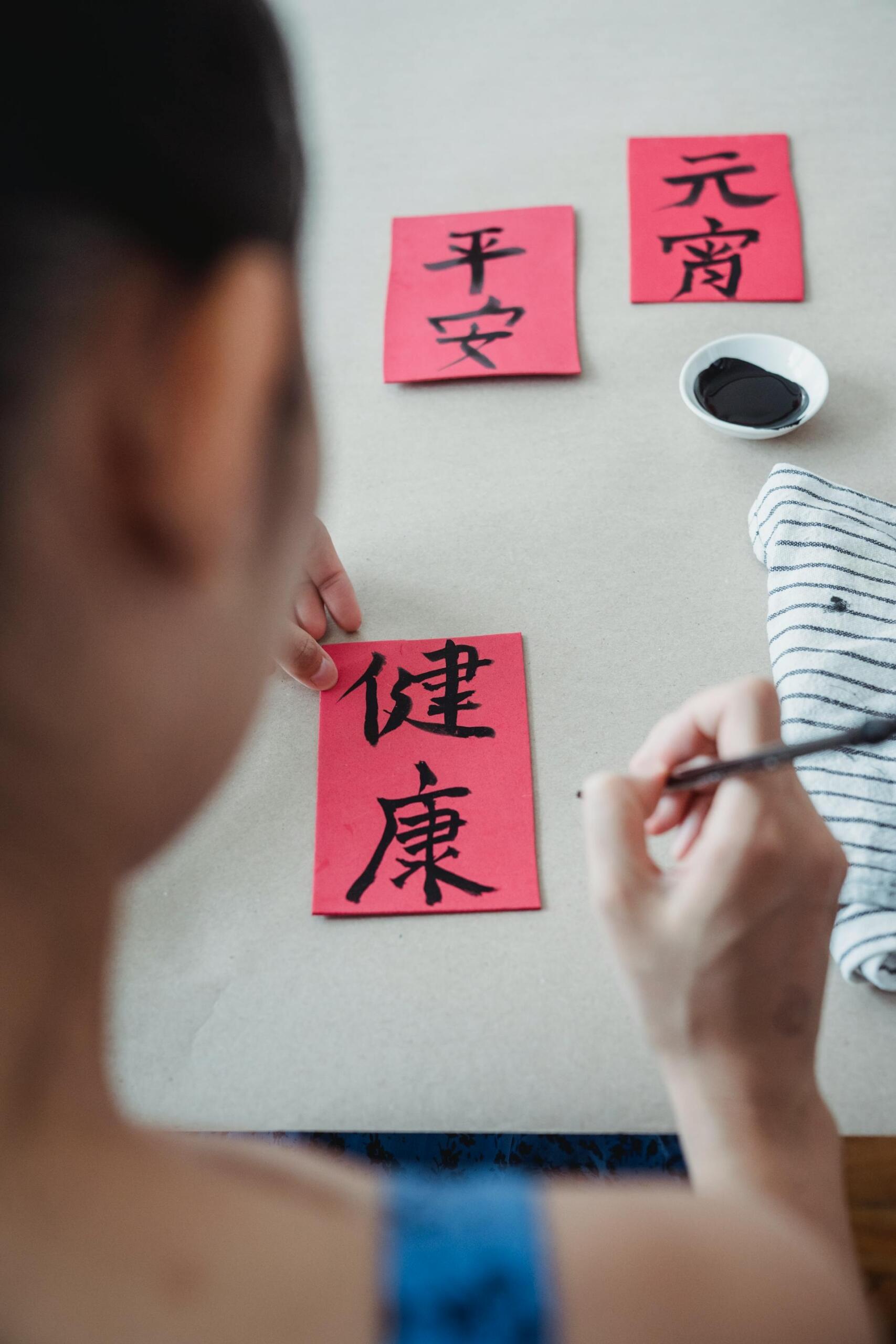 Mujer practicando caligrafía china con pincel sobre tarjetas rojas con caracteres, fotografía de Kevin Malik para Pexels