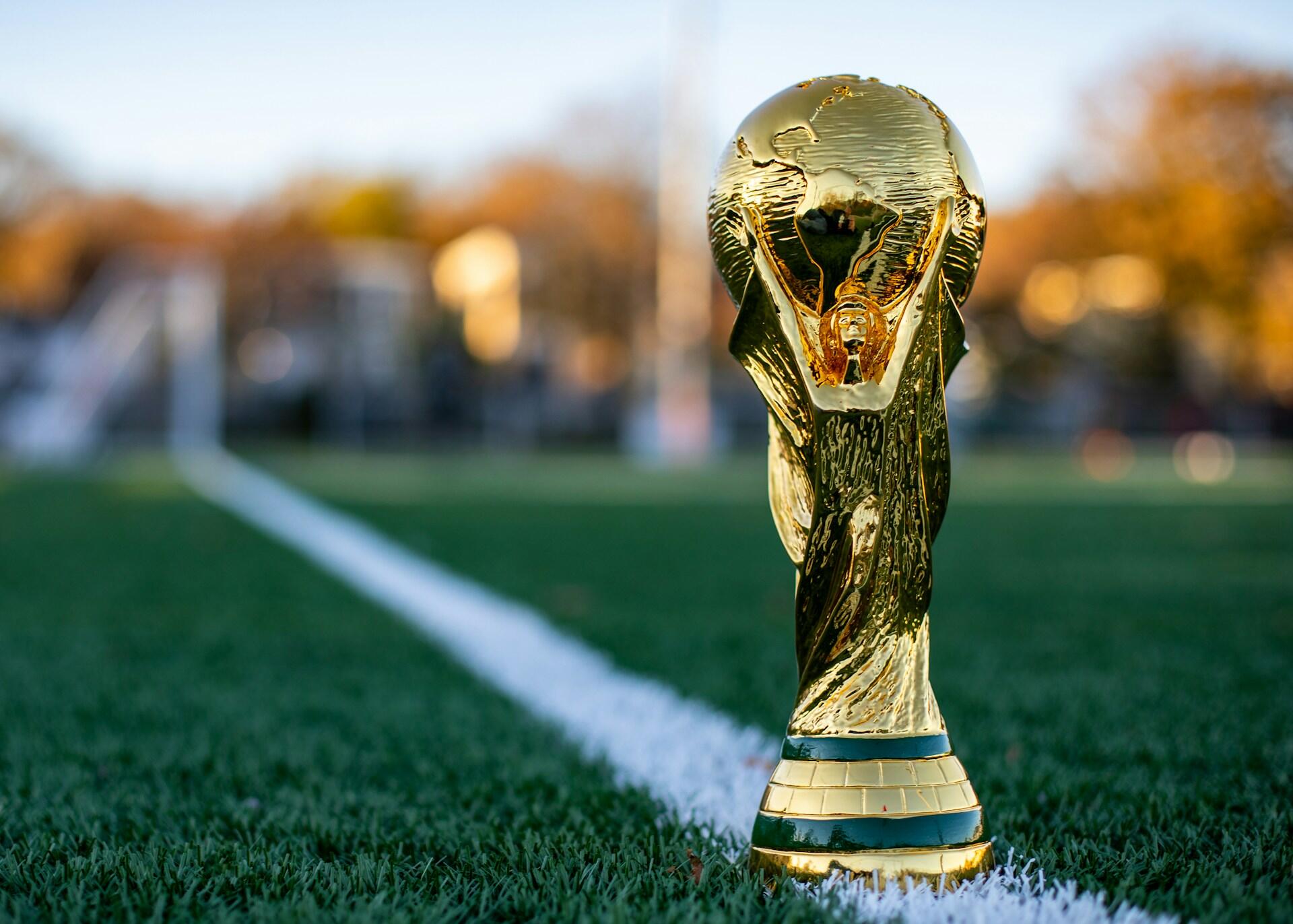 El trofeo de la Copa del Mundo de la FIFA sobre el césped de un campo de fútbol. Fotografía por My Profit Tutor.